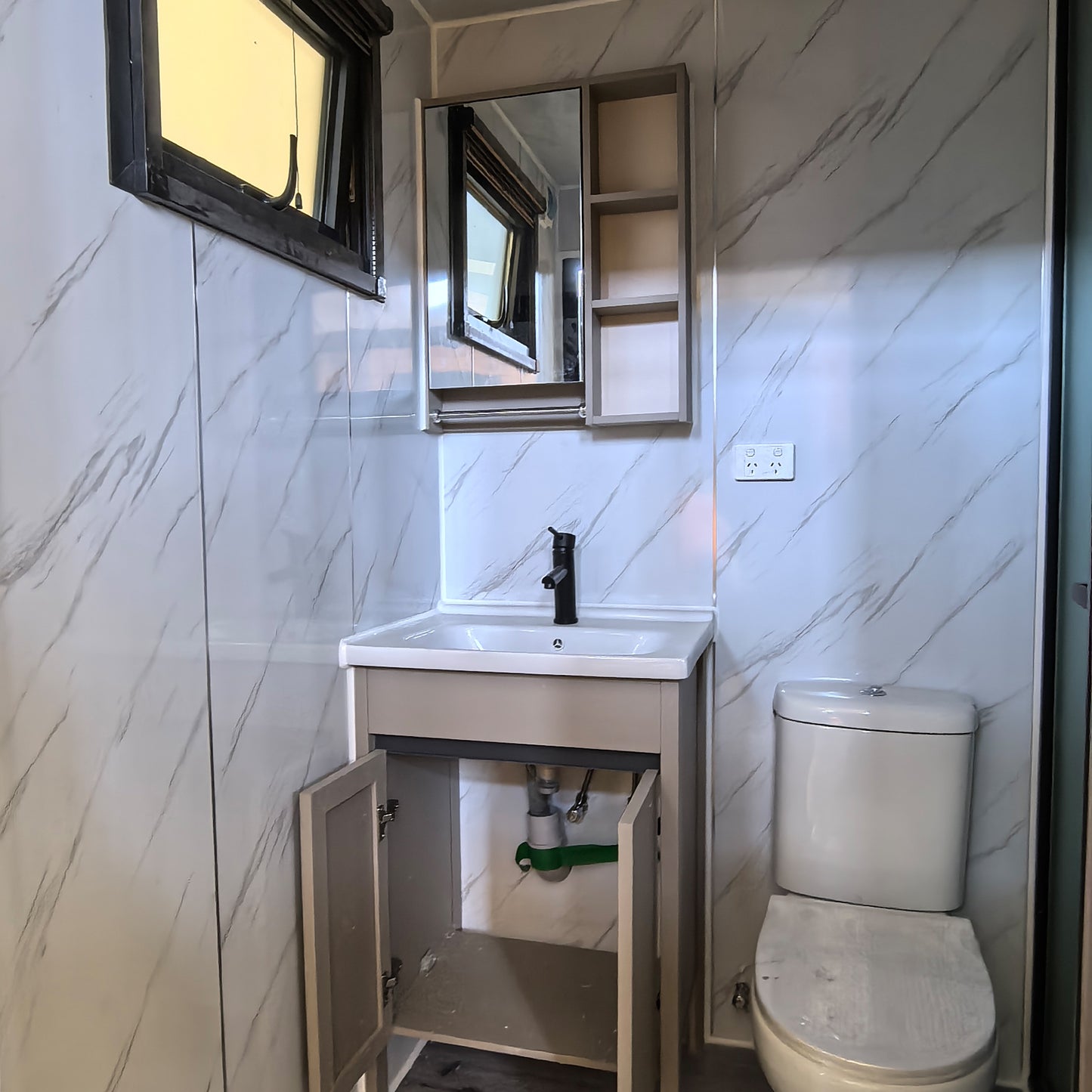 Small bathroom with toilet, sink, and mirror on a tiled wall.