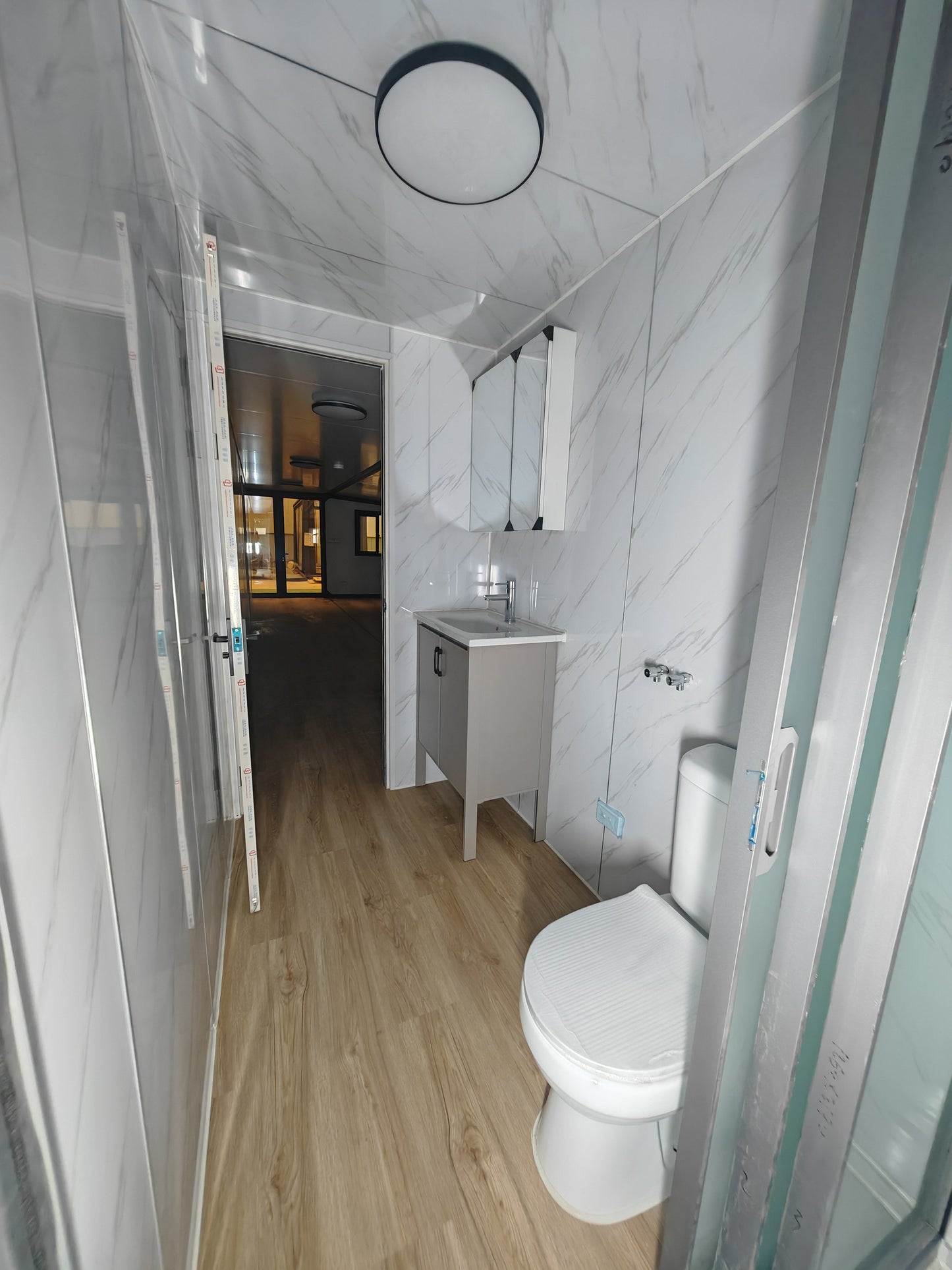 Bathroom with white toilet, sink, and cabinets on a light wood floor.