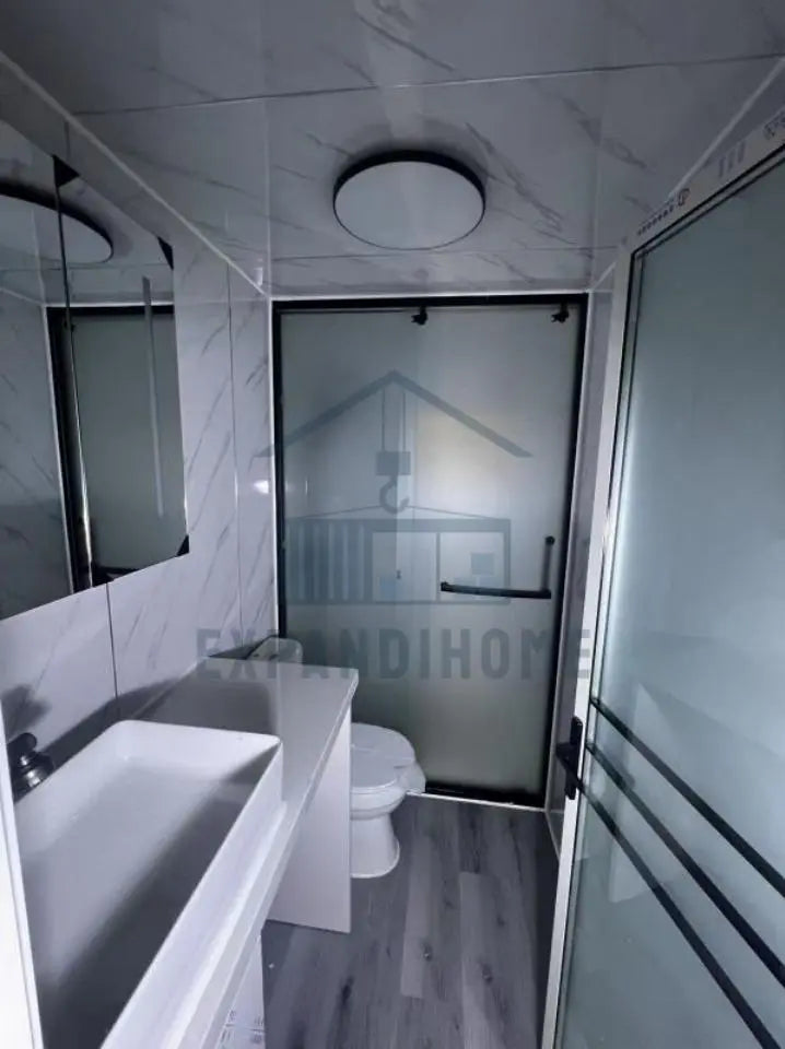 Bathroom with white tiles, sink, and toilet, featuring a real estate brand logo.