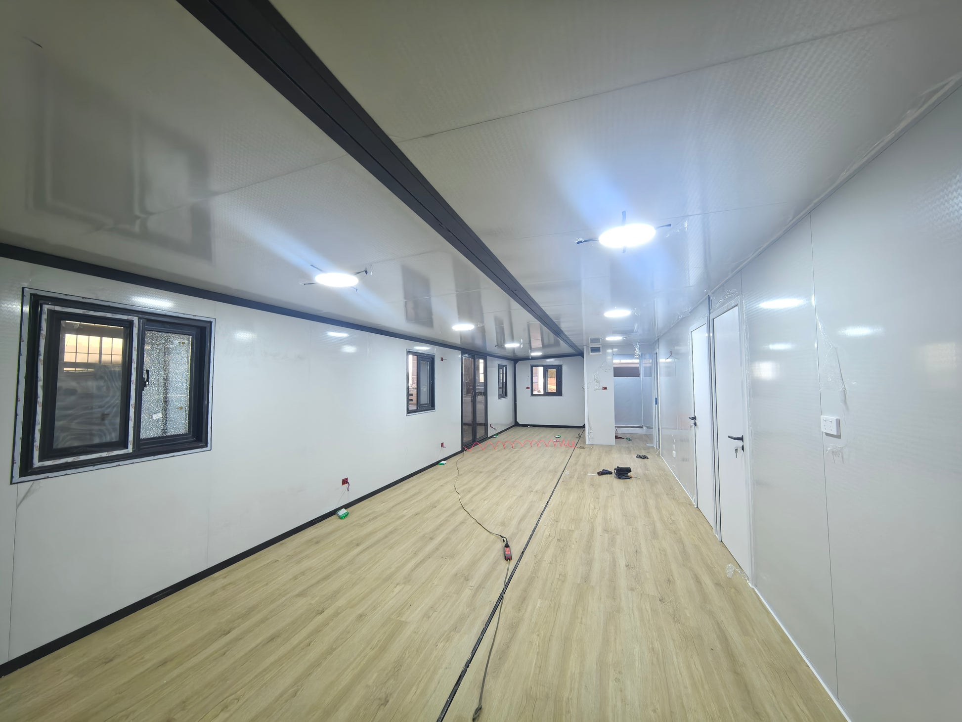 Interior of a modern shipping container home with white walls, wooden floor, and ceiling lights.