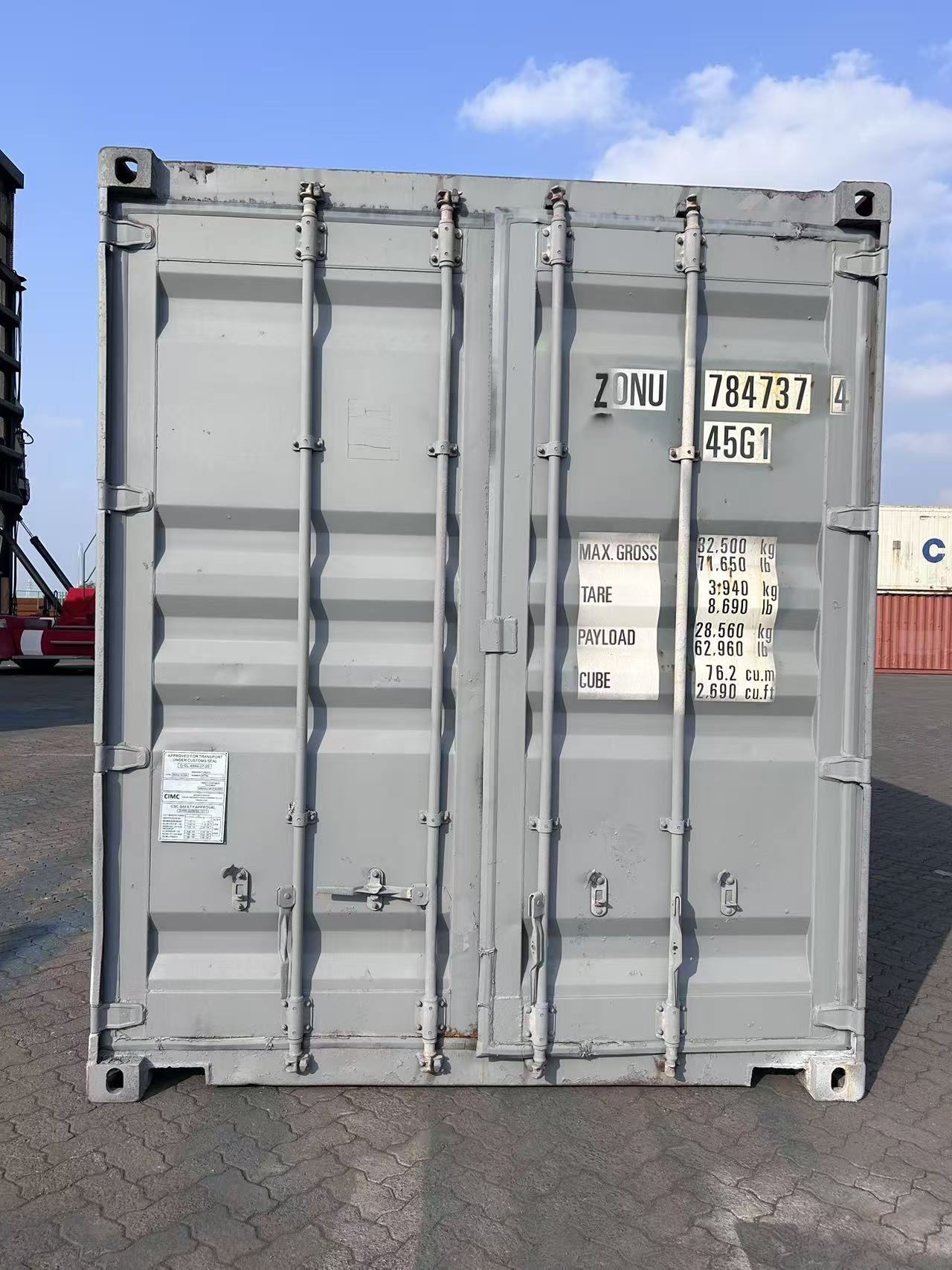 Gray shipping container with visible markings on a paved surface under a blue sky.