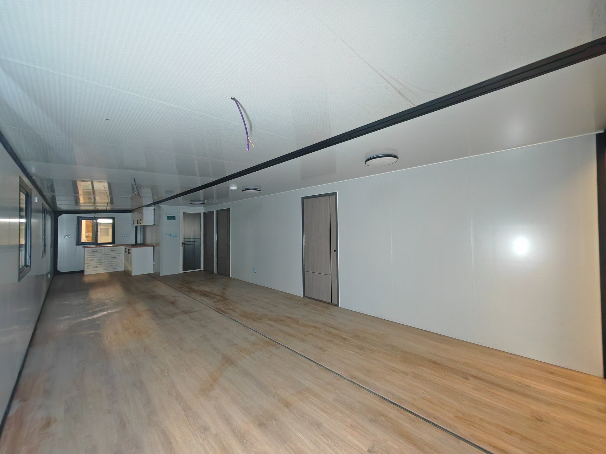 Empty room with wooden floor and white walls, possibly a shipping container conversion.