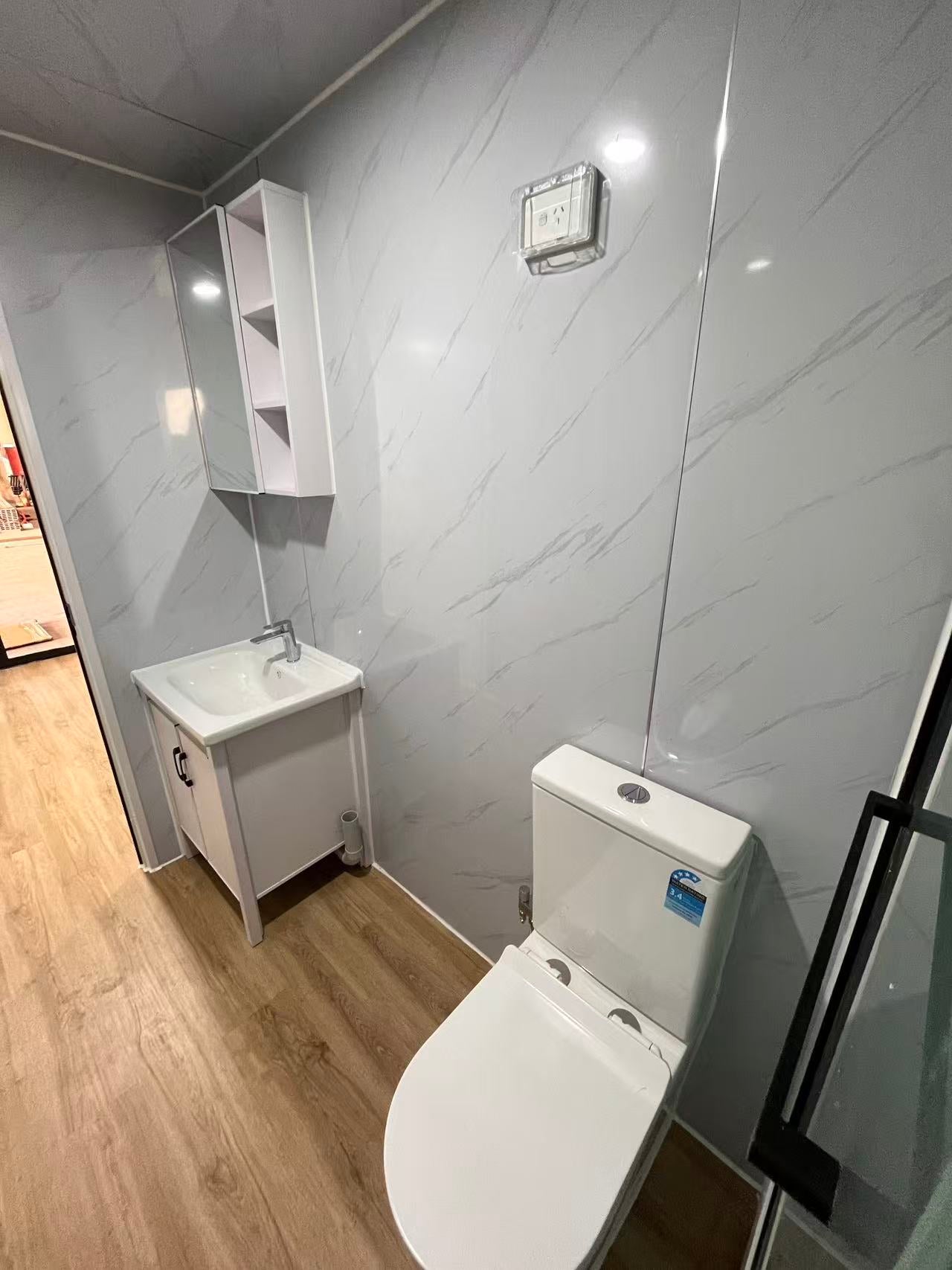 Bathroom with white toilet and sink against a gray tiled wall.