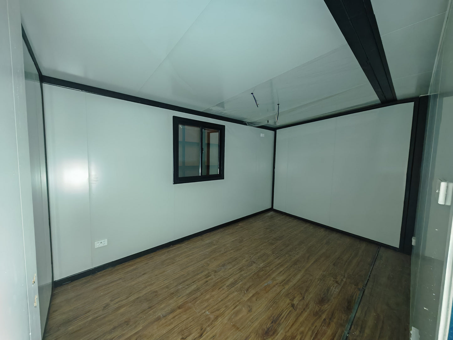 Empty room with white walls, wooden floor, and a small window.