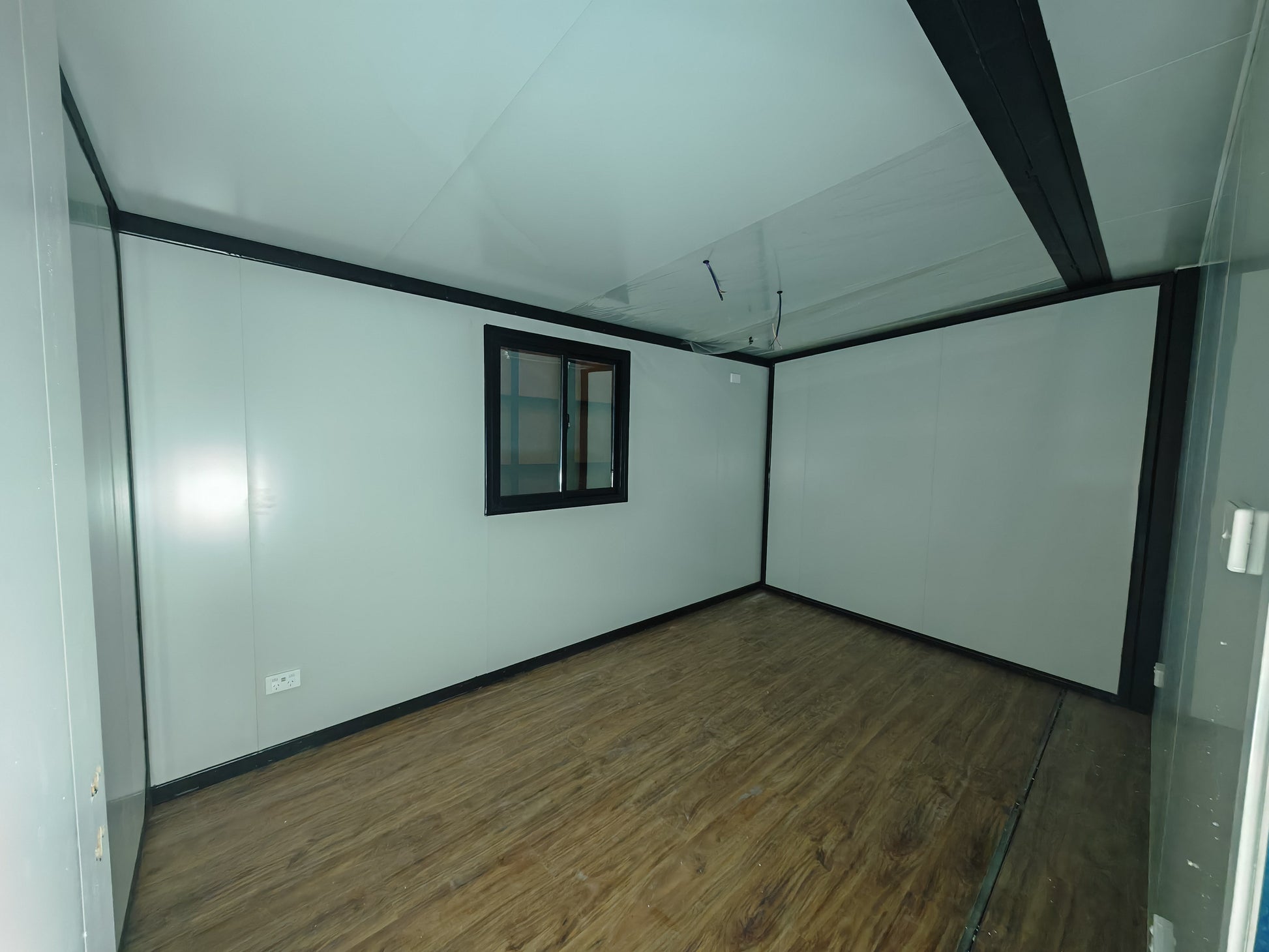 Empty room with white walls, wooden floor, and a small window.