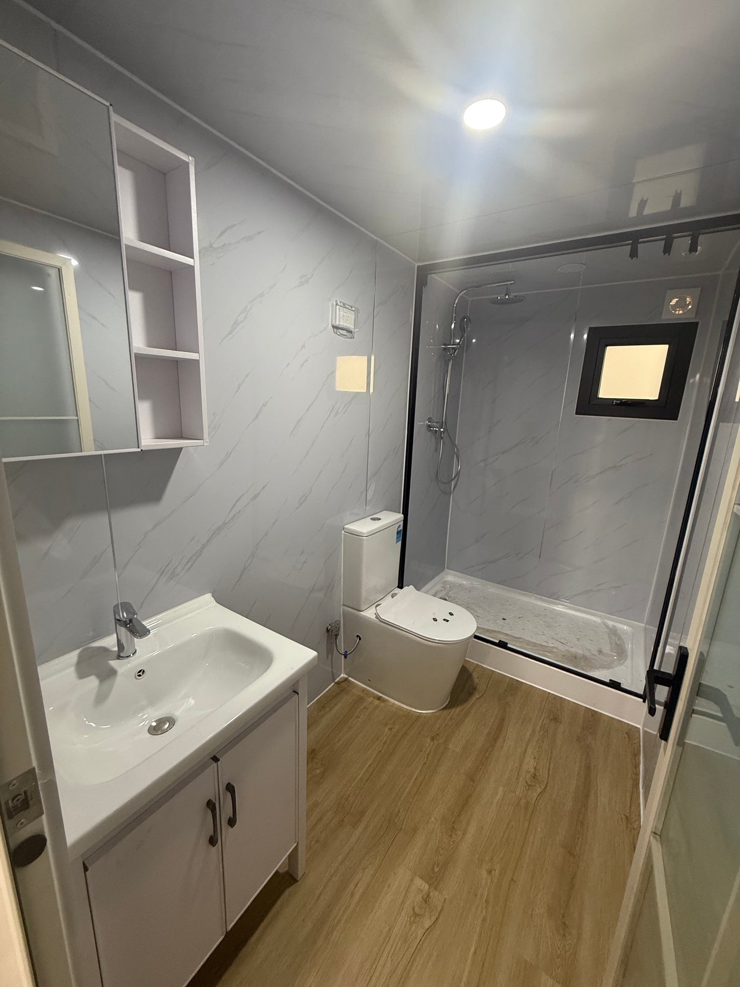 Compact living space with a bed, desk, and sink in a small room.