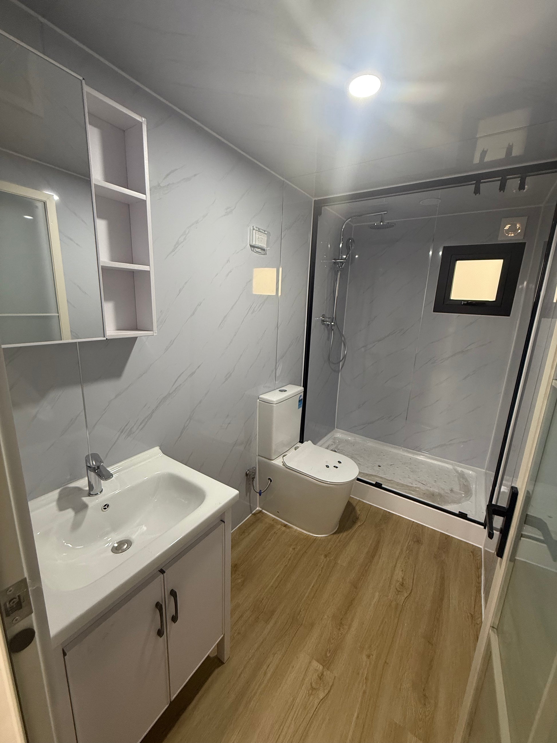 Compact living space with a bed, desk, and sink in a small room.