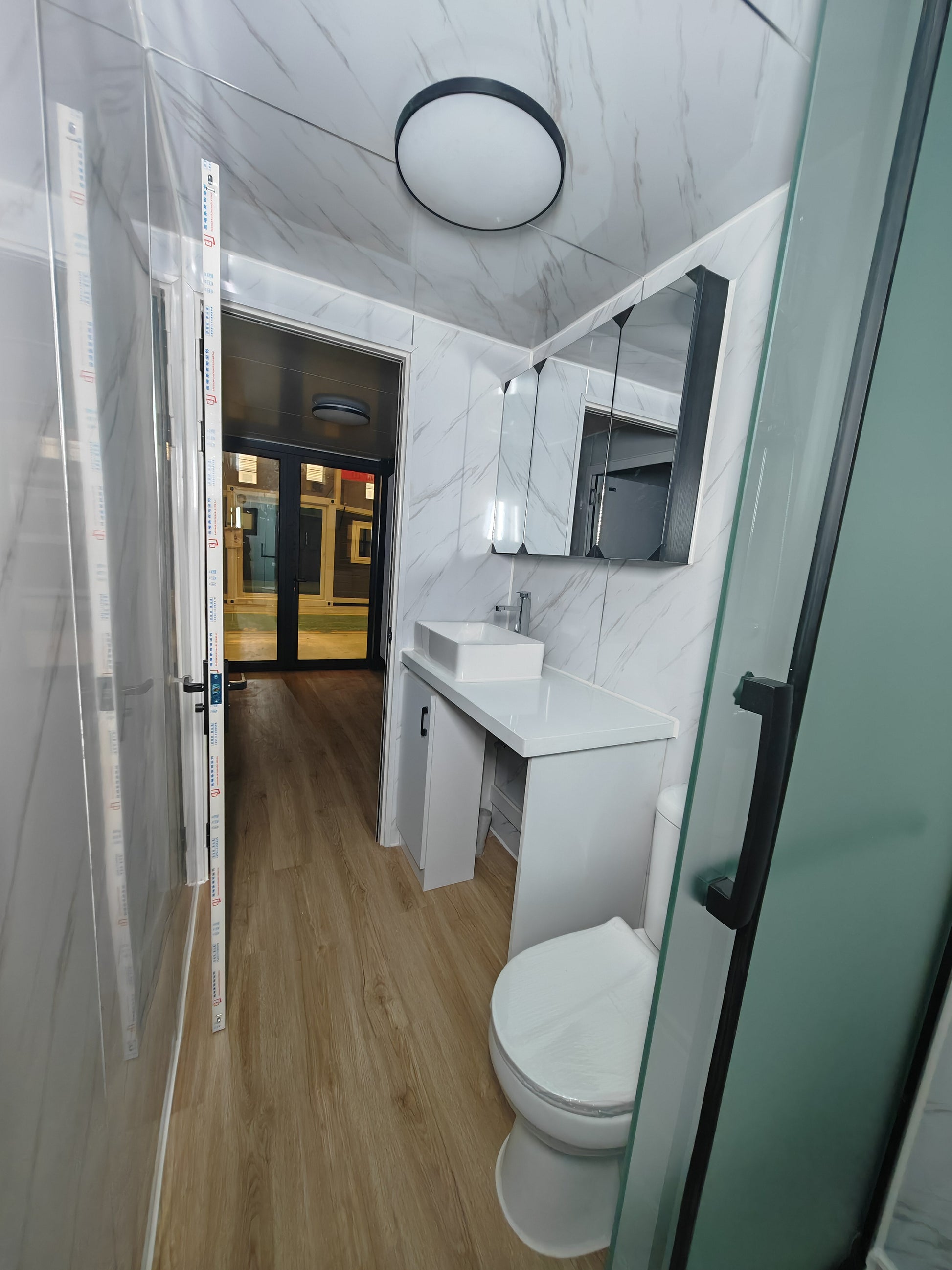 Modern bathroom with white marble walls, a toilet, sink, and shower.