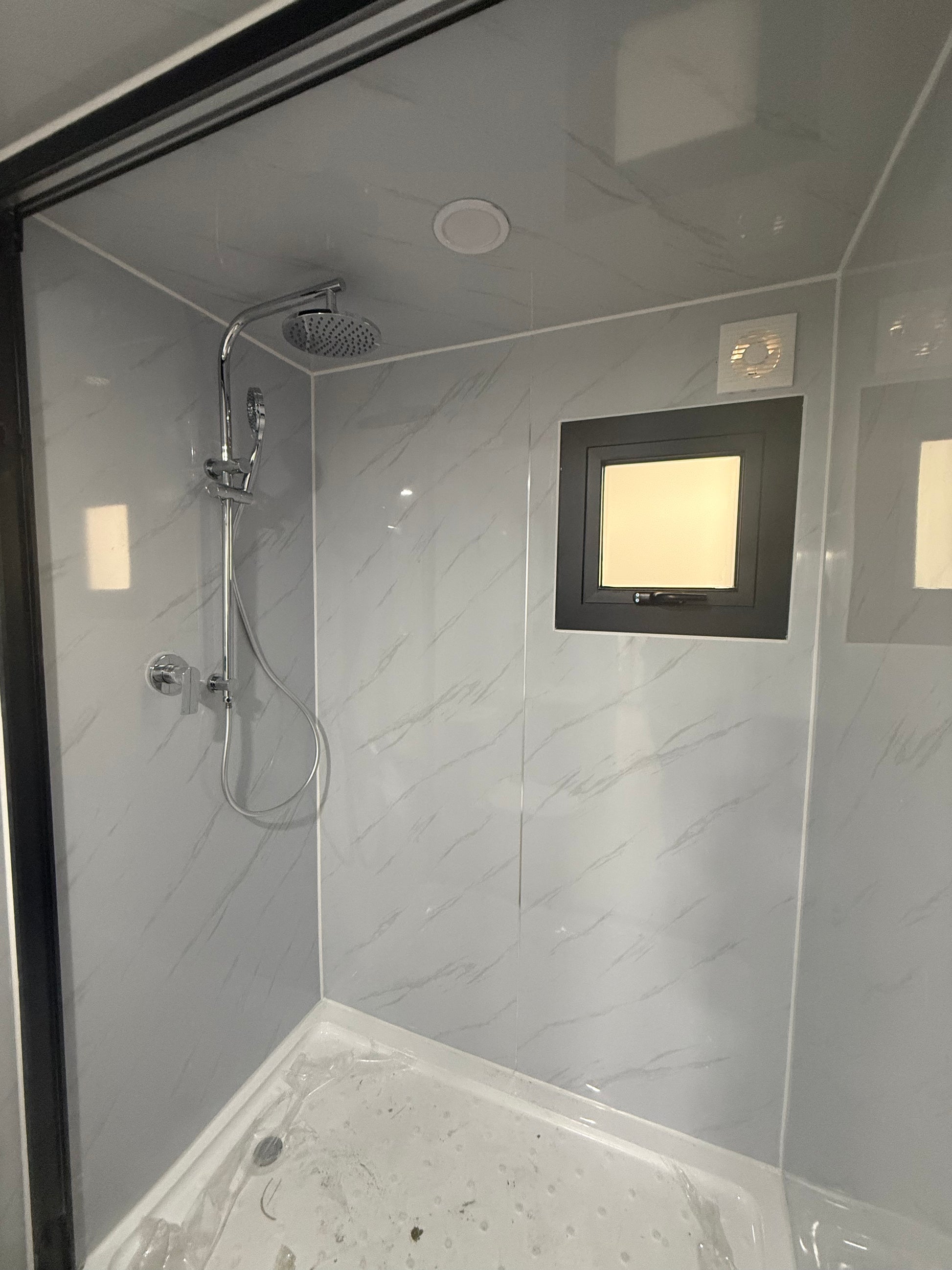 Modern shower cabin with tiled walls and a skylight.