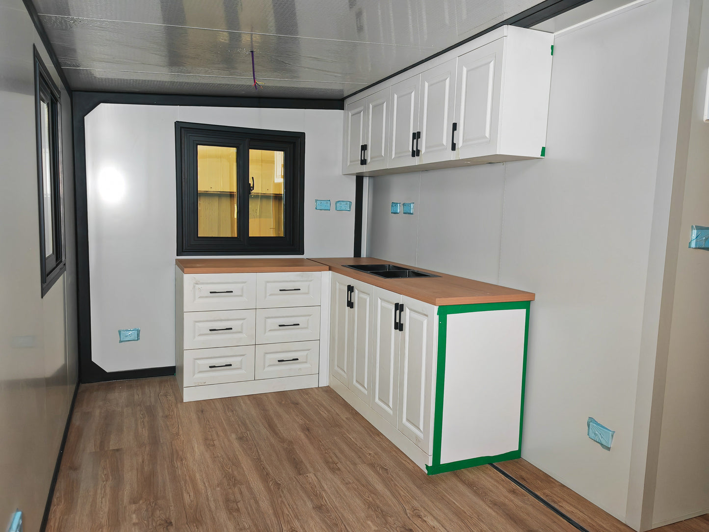 Small kitchenette with white cabinets, wooden countertop, and window on a white wall.