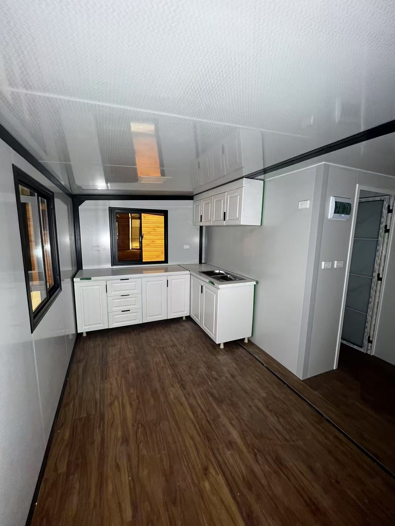Small kitchenette with white cabinets and wooden floor in a compact living space.