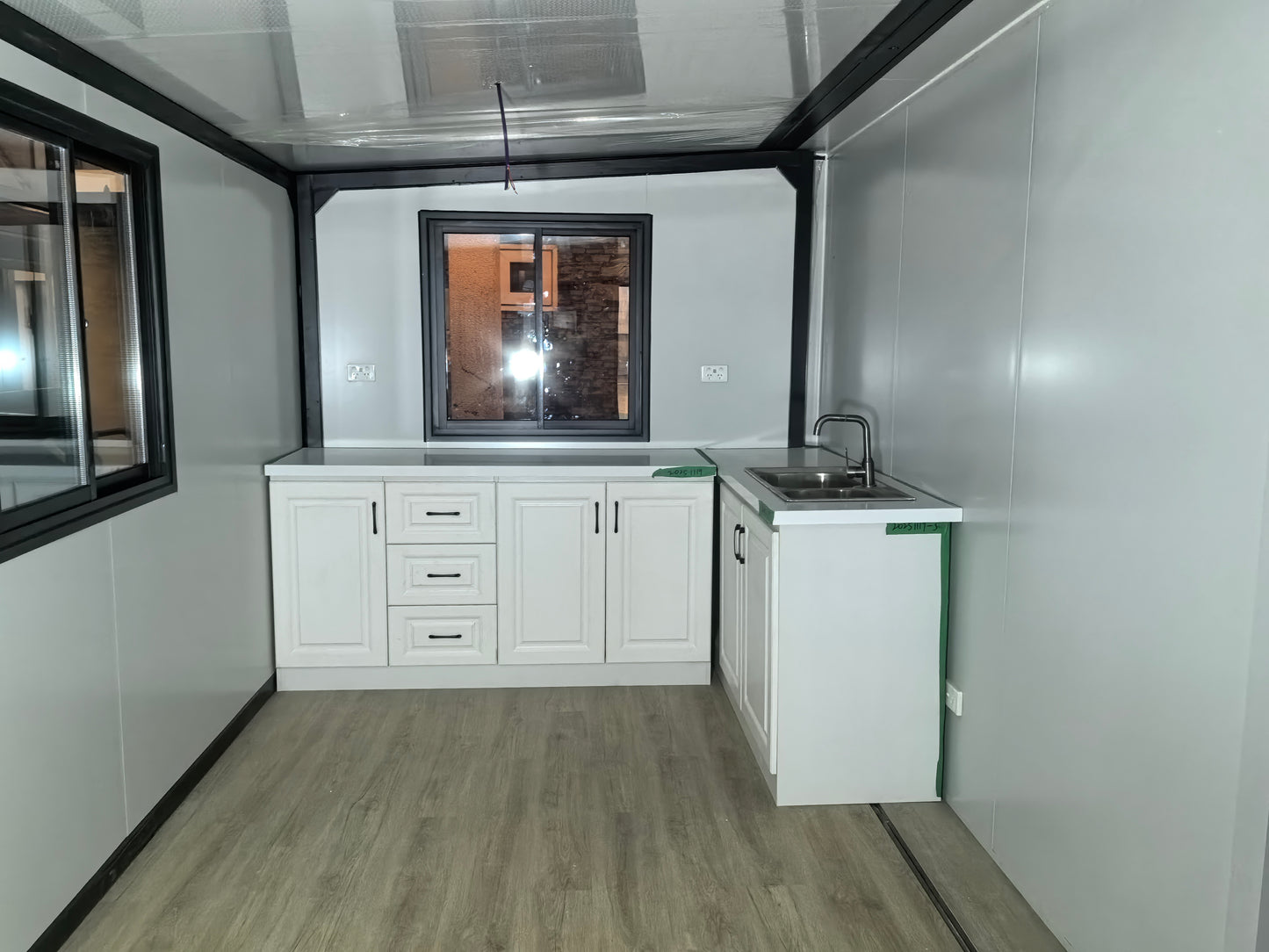 Small kitchenette with white cabinets, sink, and window in a compact living space.