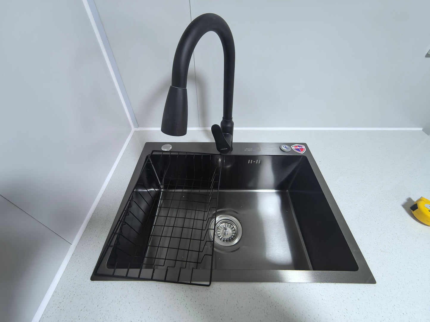 Stainless steel kitchen sink with black faucet on a white tiled wall