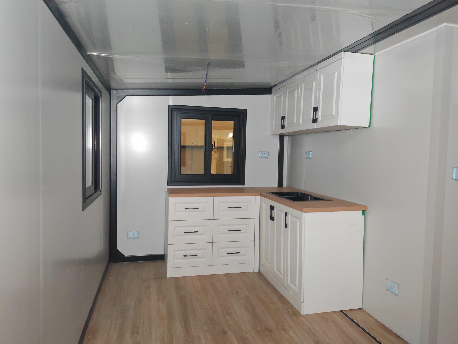 Small kitchenette with white cabinets, wooden countertop, and black-framed window.