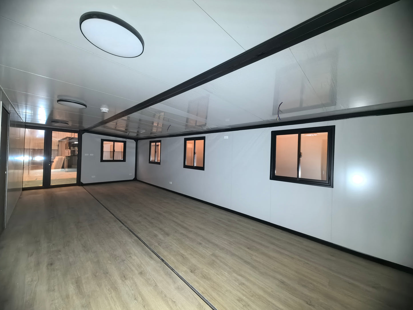 Modern  space with white walls, wooden flooring, and large windows .