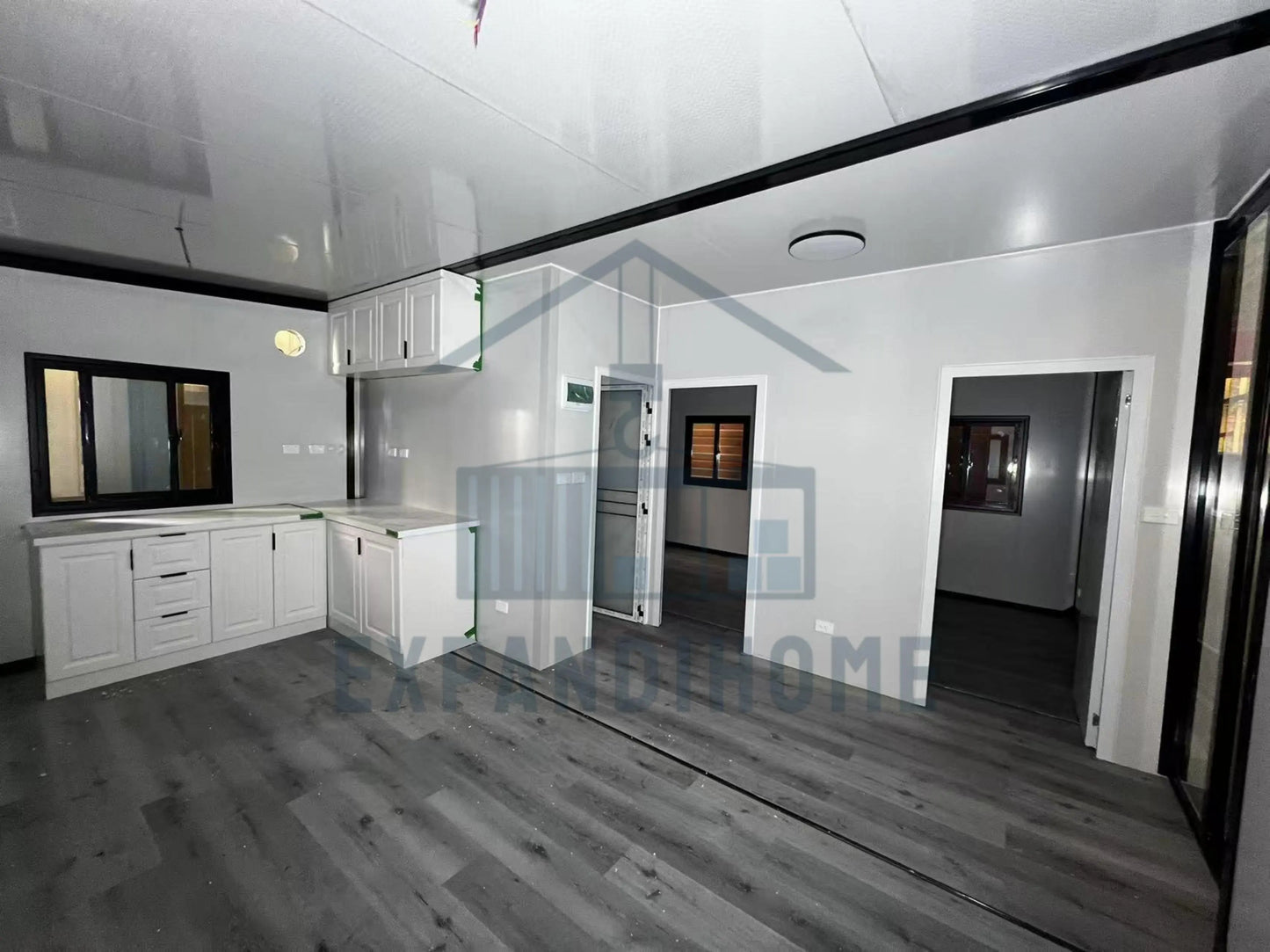 Modern kitchen with white cabinets and gray flooring, featuring the Expand Home logo.