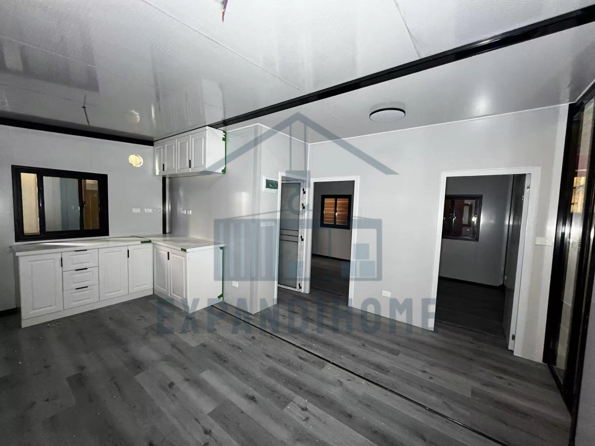 Modern kitchen with white cabinets and gray flooring, featuring the Expand Home logo.