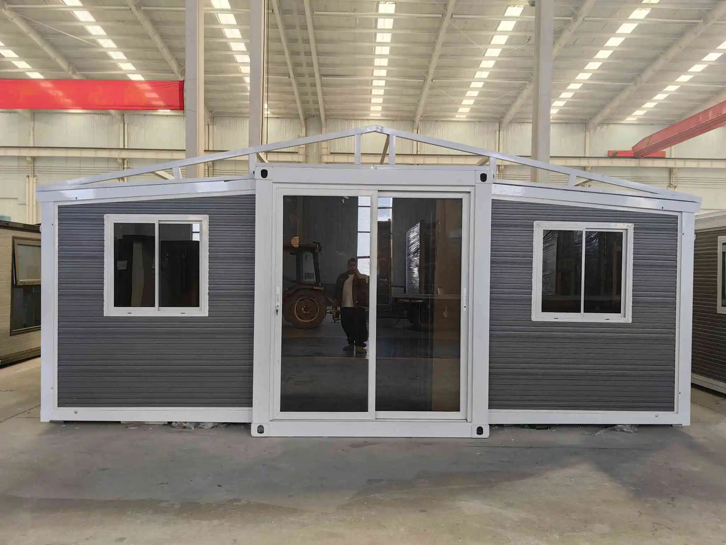 A 20ft expandable house featuring two bedrooms, one bathroom, and one kitchen, with a gray exterior and visible glass doors and windows.