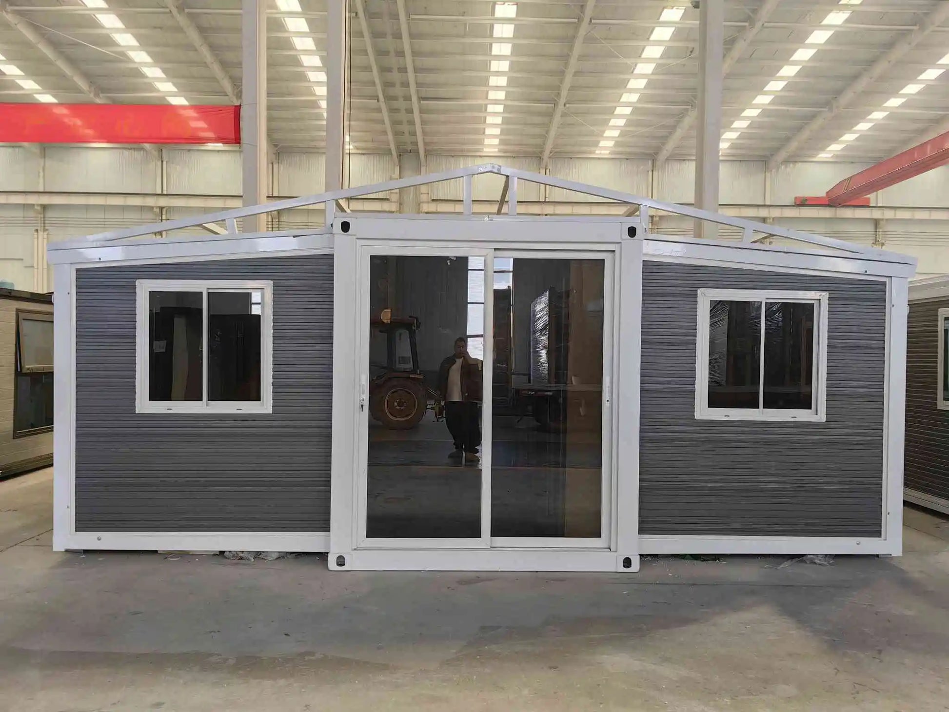 A 20ft expandable house featuring two bedrooms, one bathroom, and one kitchen, with a gray exterior and visible glass doors and windows.