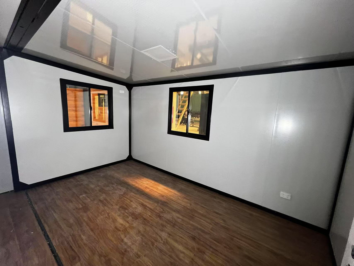 Small room with white walls, wooden floor, and two small windows.