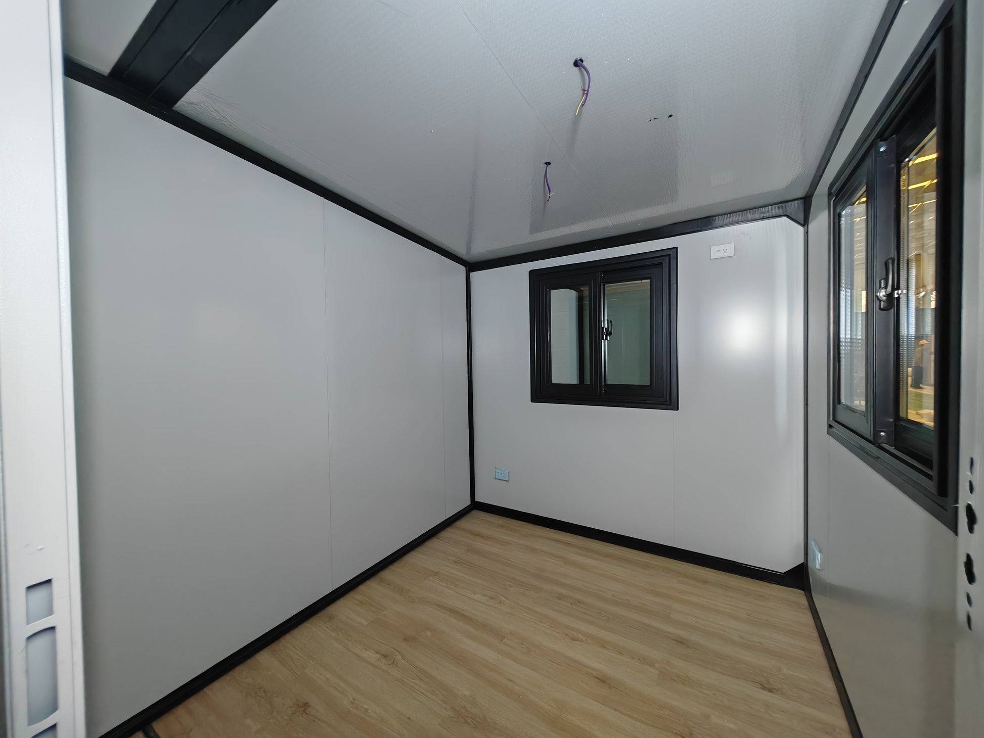Small room with white walls, wooden floor, and two glass windows.