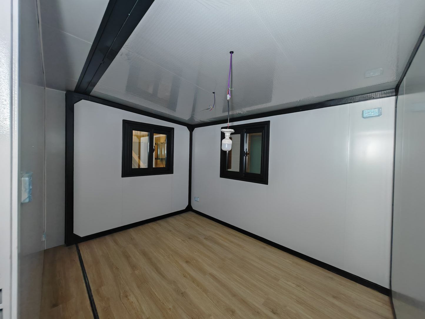 Small room with white walls, wooden floor, and two small windows.