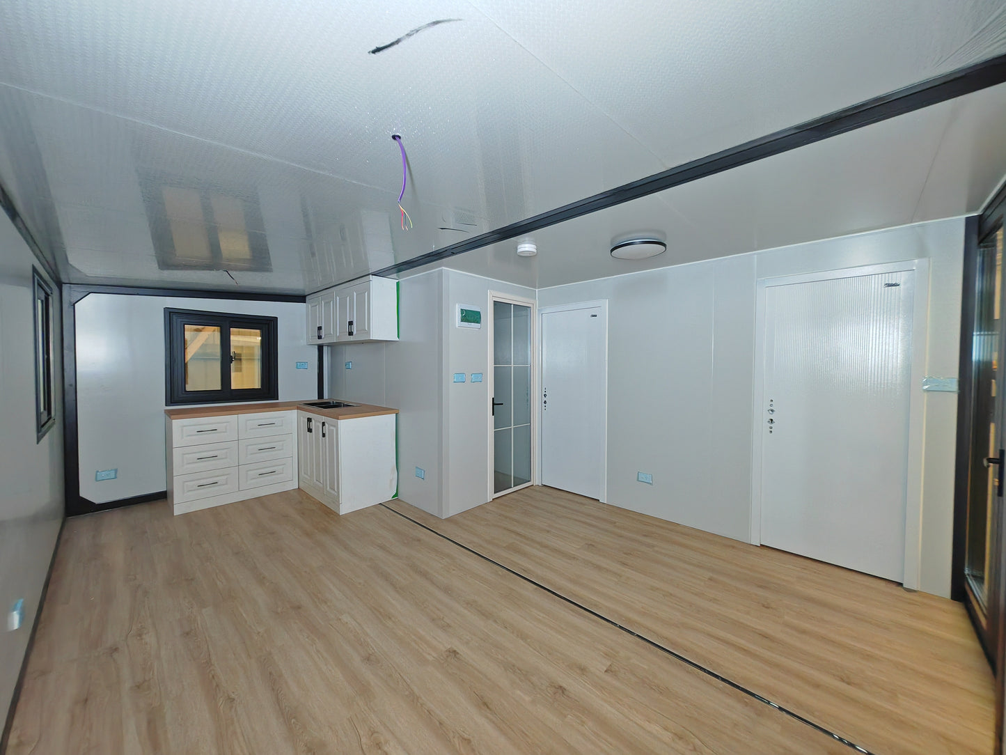 Modern kitchen with wooden flooring and white cabinets.