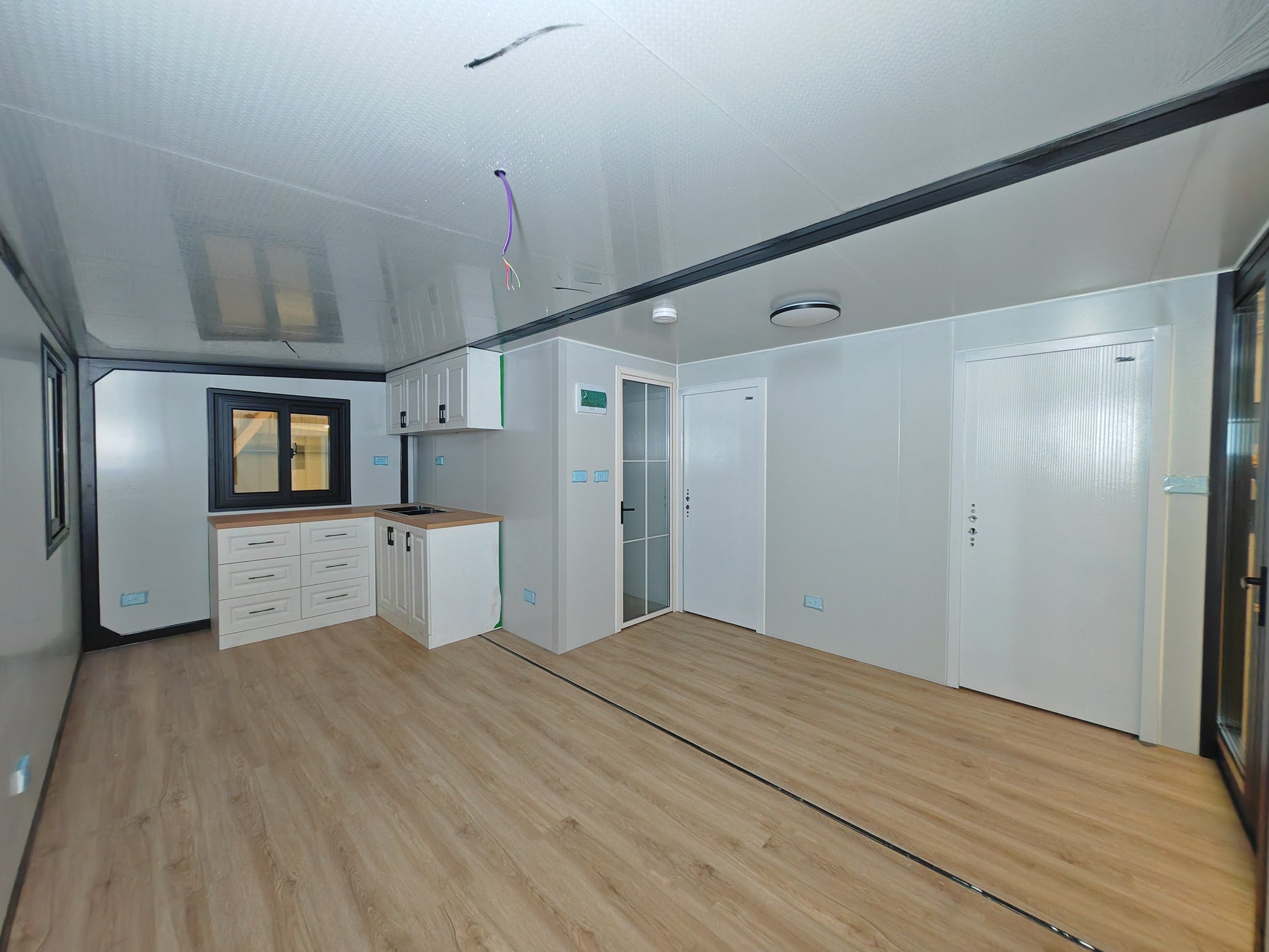 Modern kitchen with wooden flooring and white cabinets.