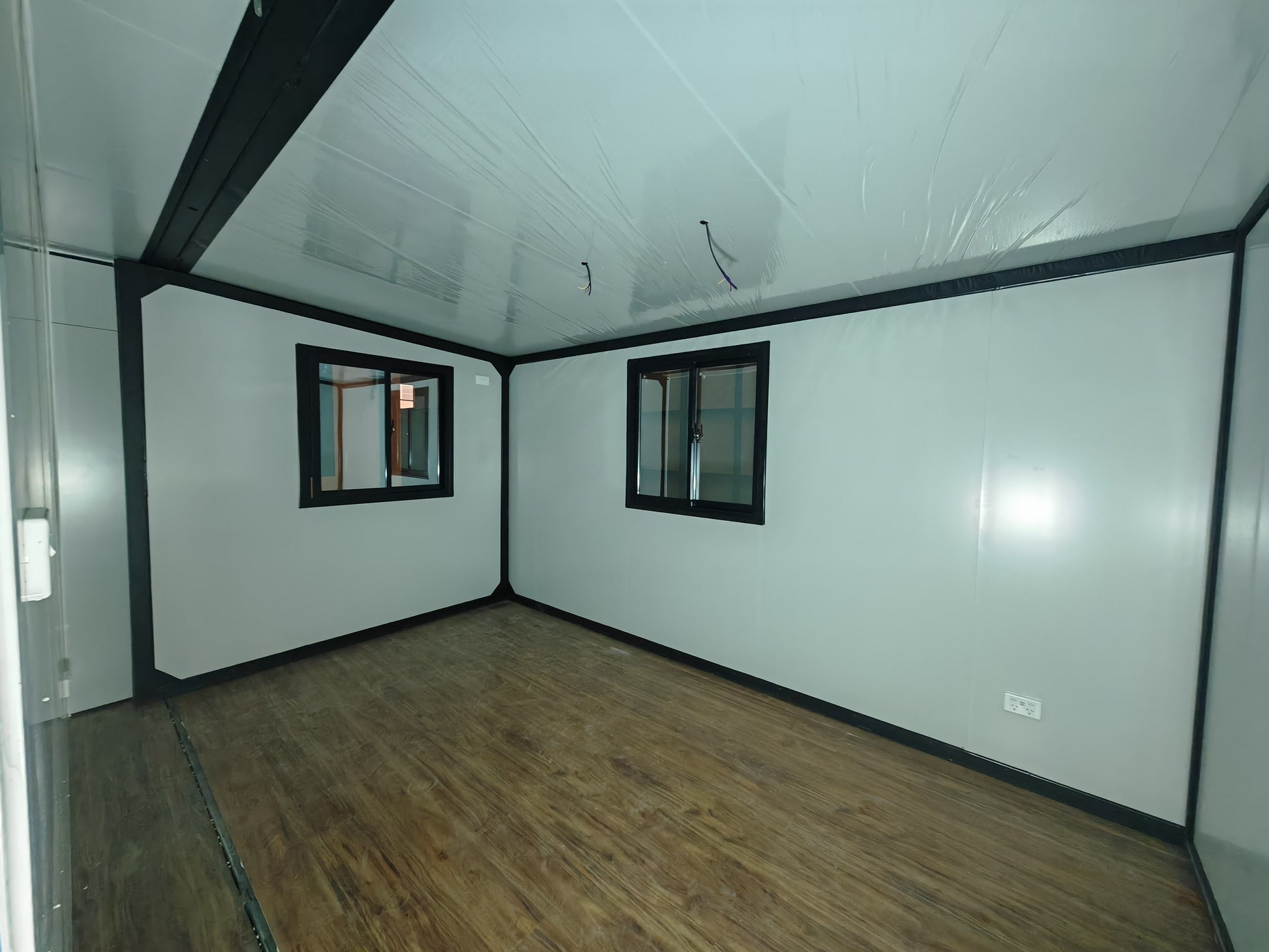 Empty room with white walls, wooden floor, and two small windows.