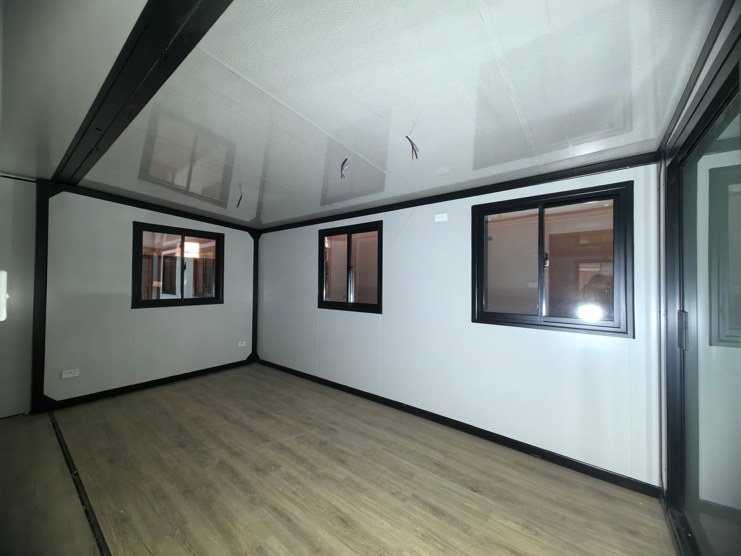 Empty room with white walls, wooden floor, and large windows.