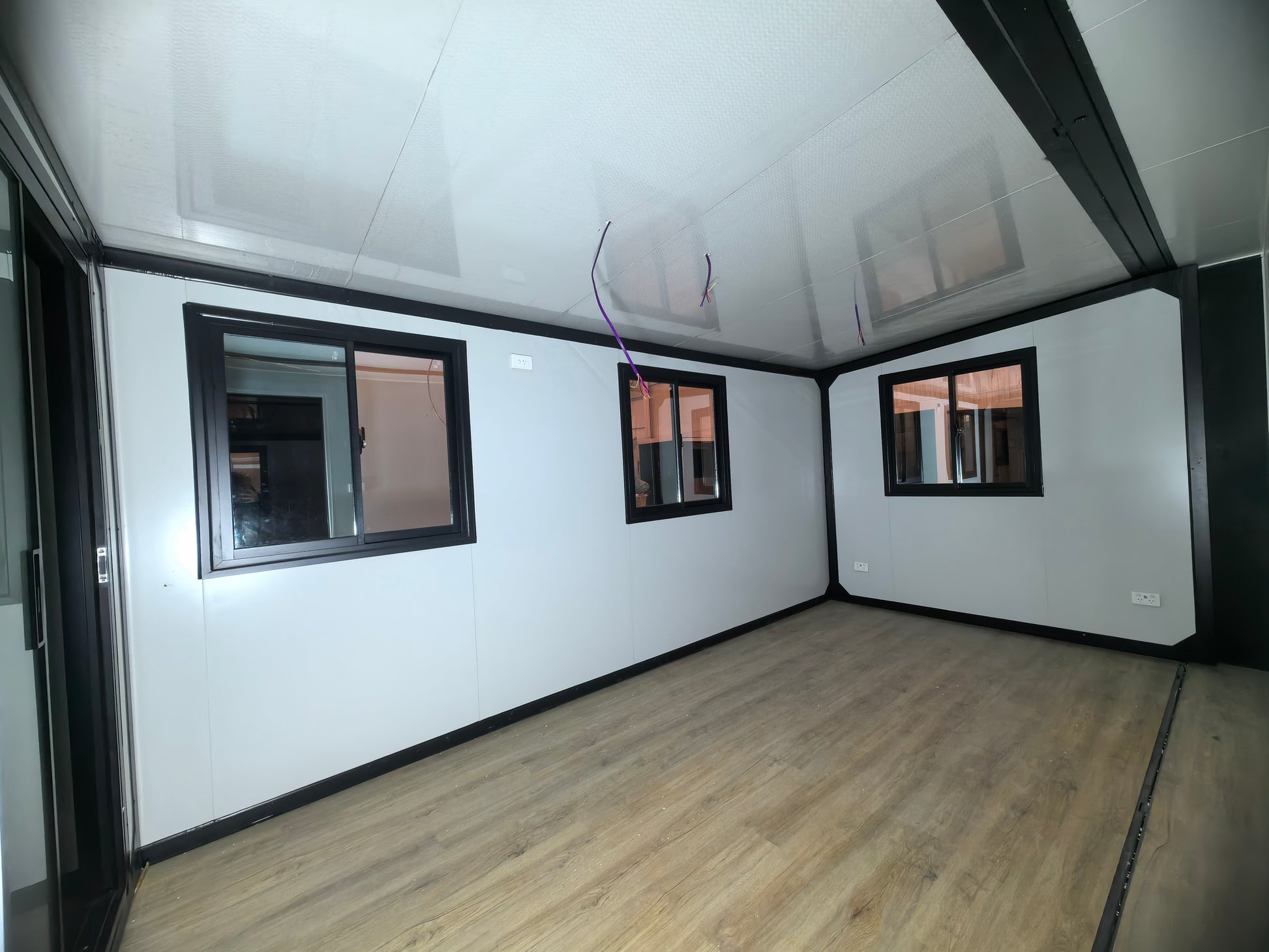 Empty room with white walls, wooden floor, and windows.