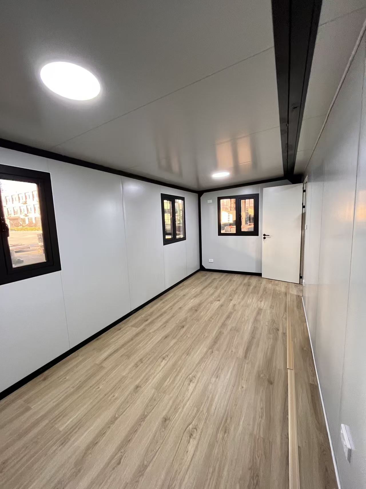 Small room with white walls, wooden floor, and windows.