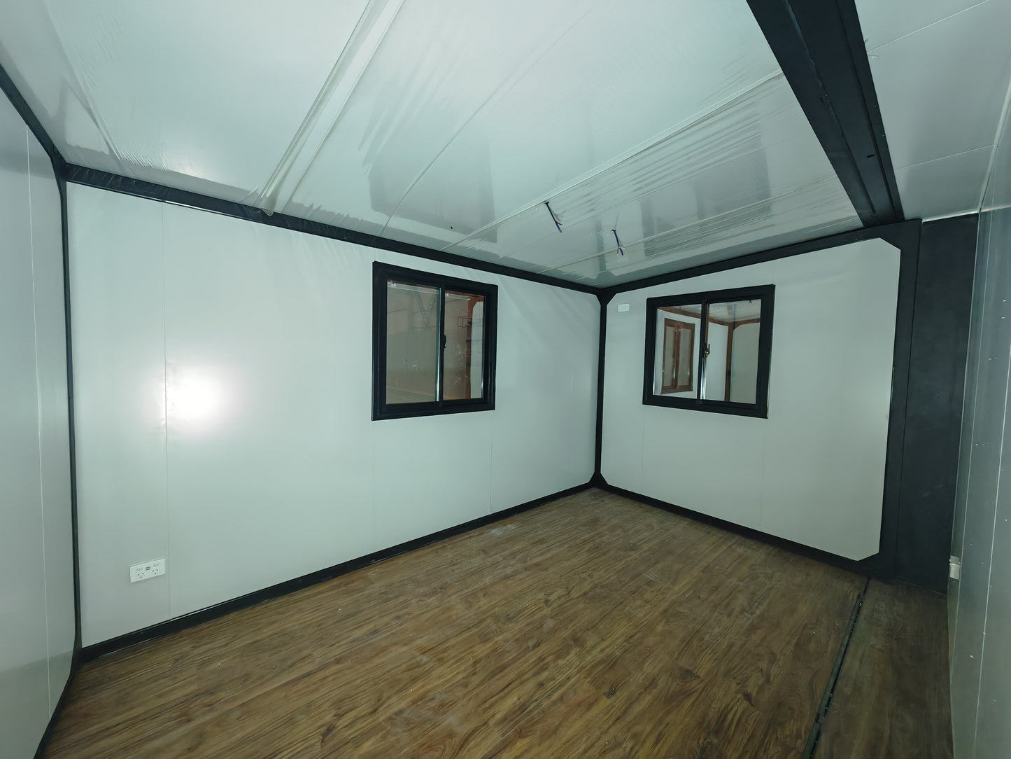 Empty room with white walls, wooden floor, and two small windows.