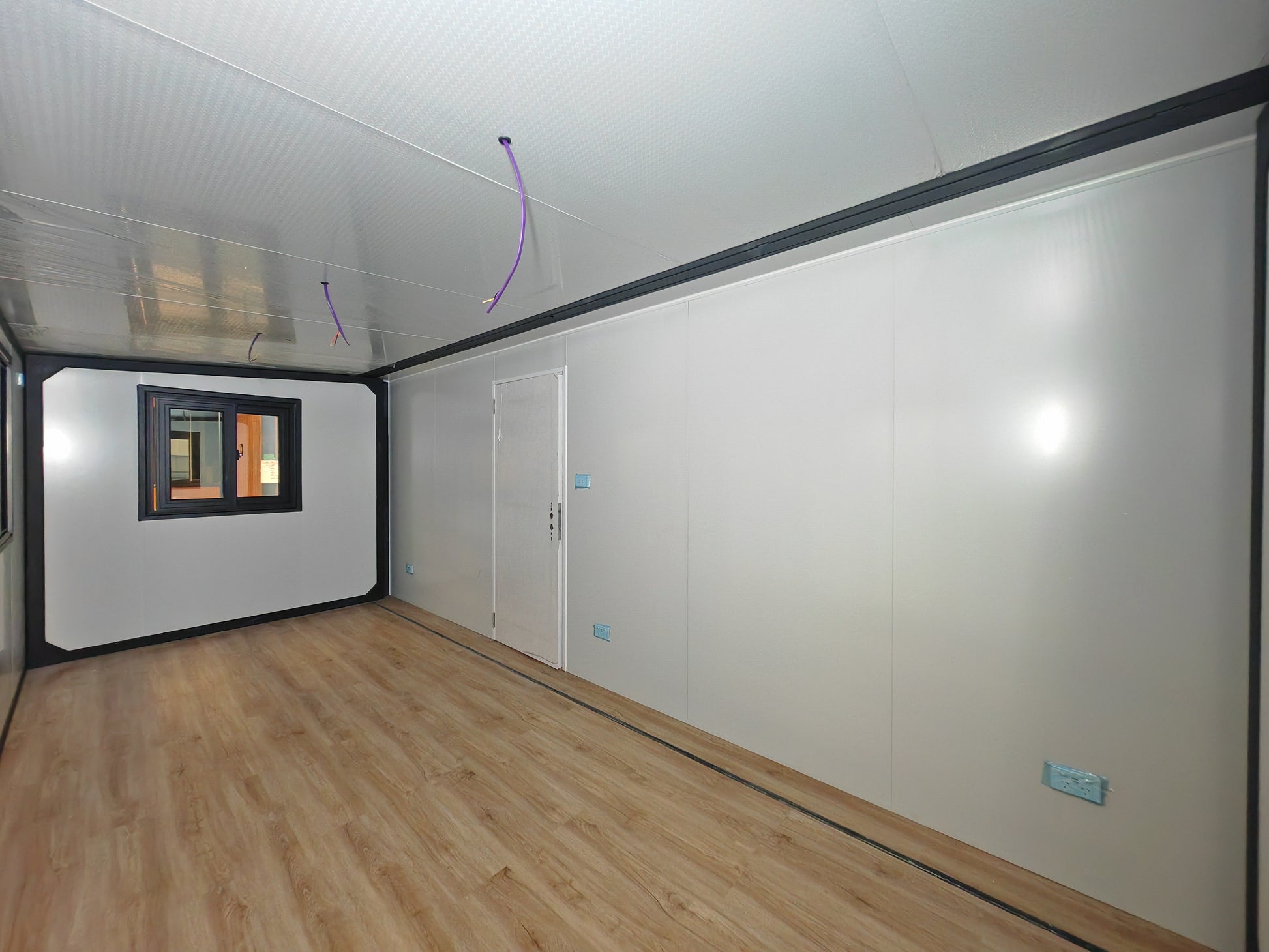 Empty room with white walls, wooden floor, and a small window.