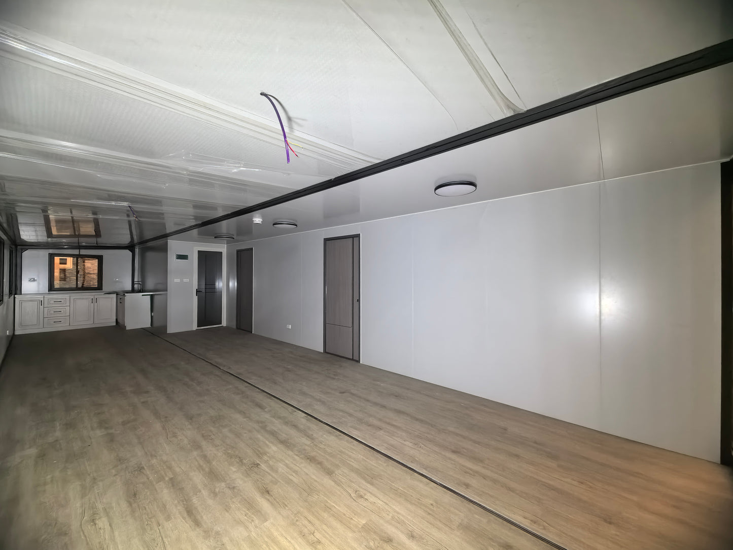 Empty room with white walls, wooden floor, and ceiling lights.