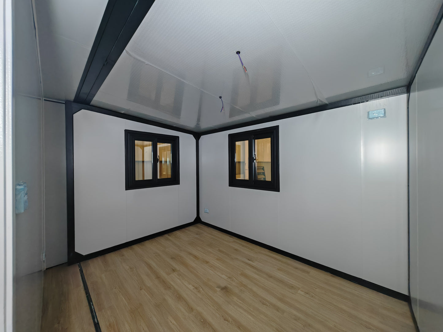 Small room with white walls, a wooden floor, and two windows.