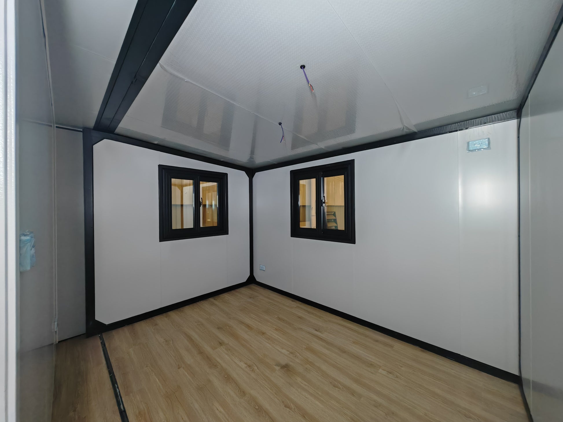 Small room with white walls, a wooden floor, and two windows.