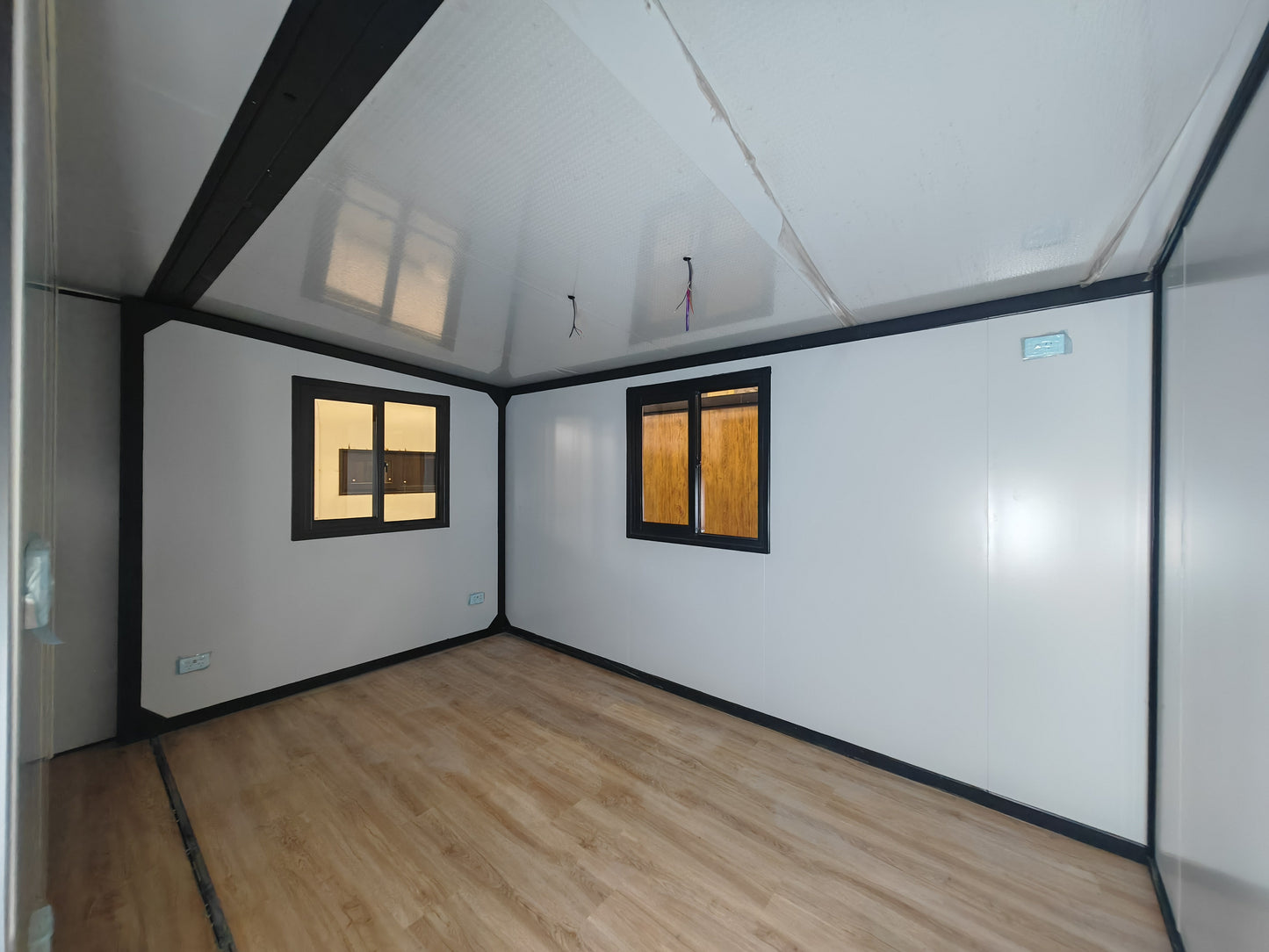 Small room with white walls, wooden floor, and two windows.