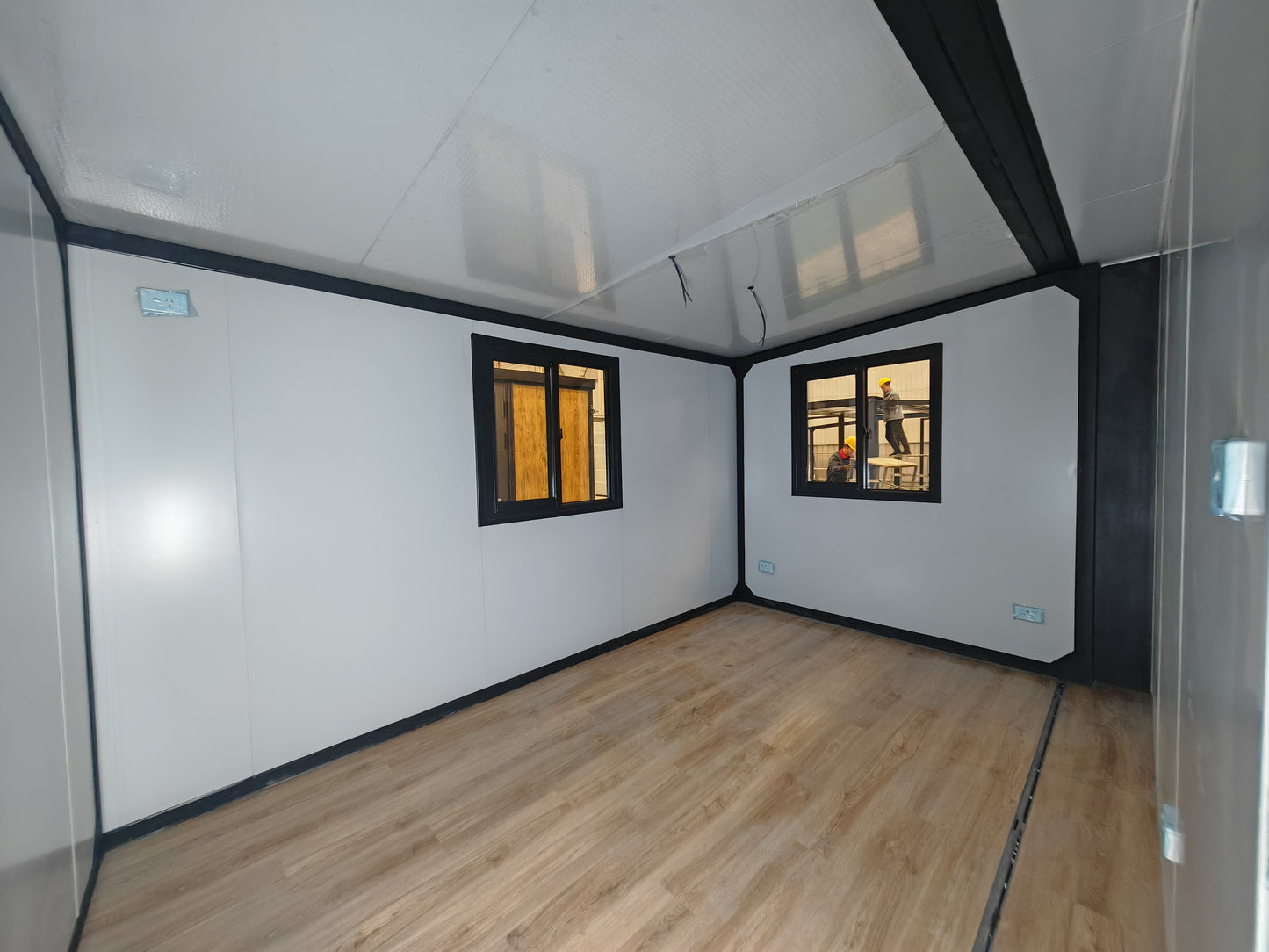 Small room with white walls, wooden floor, and two windows.