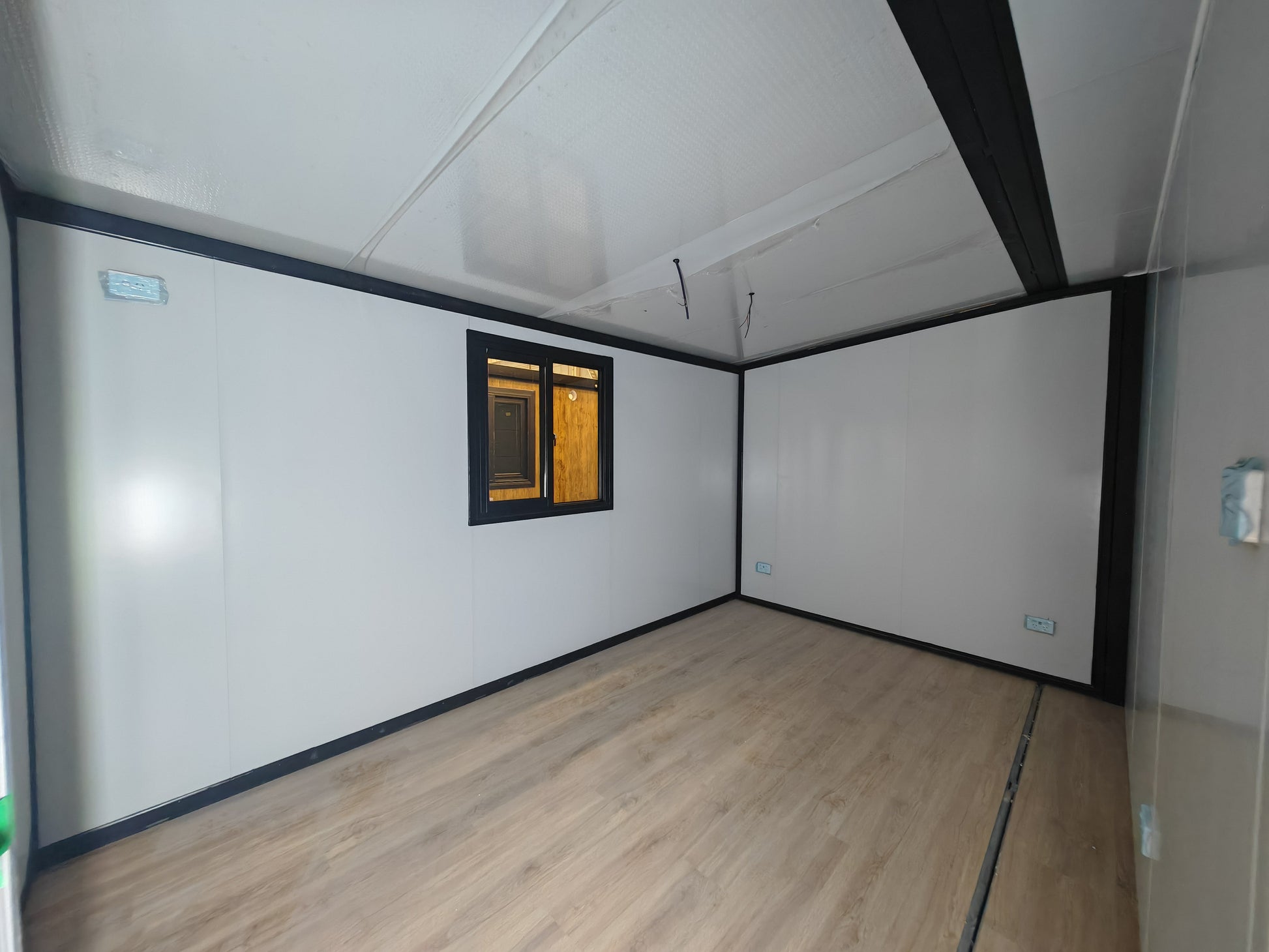 Empty room with white walls, wooden floor, and a small window.