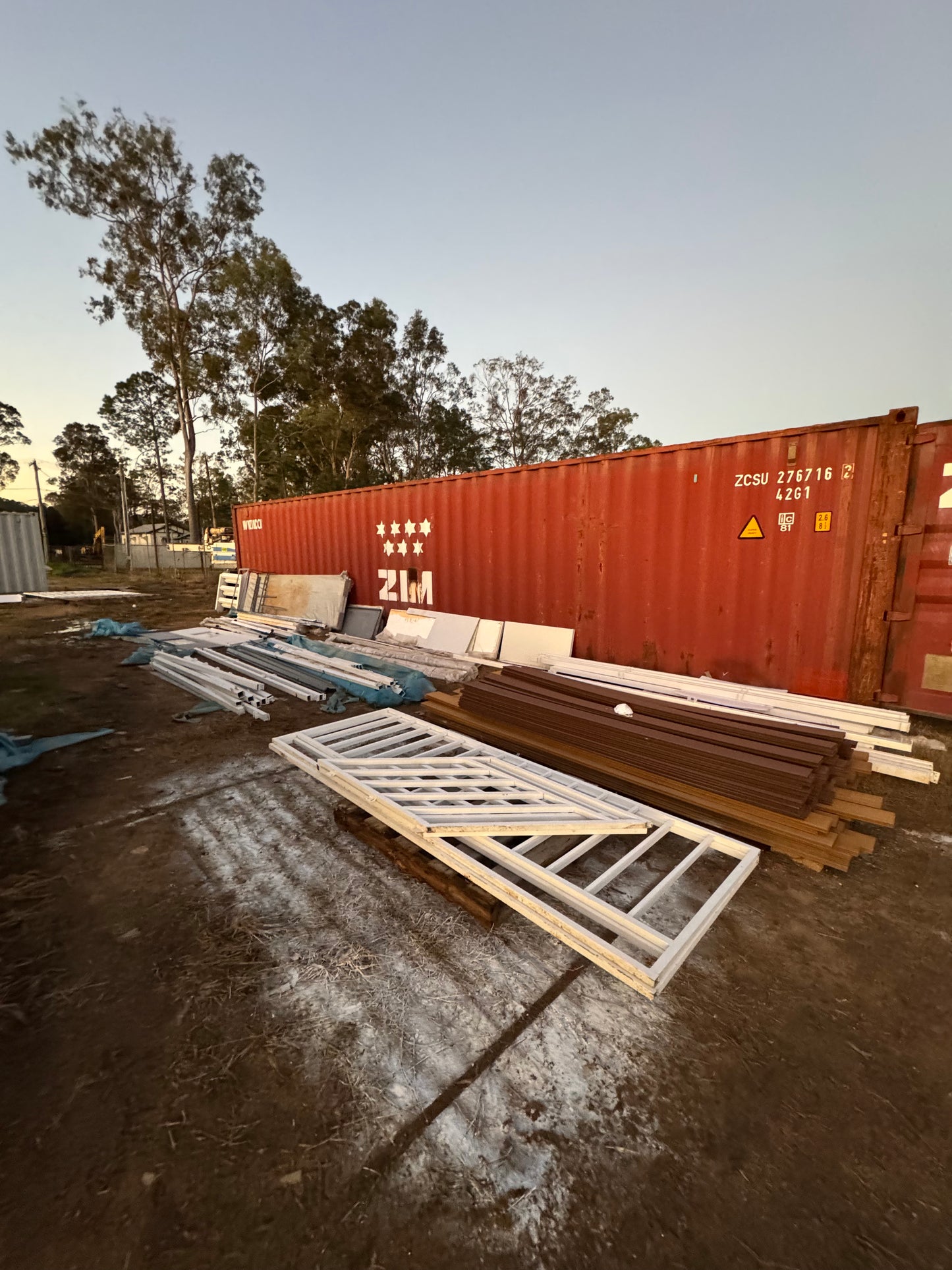 Red shipping container with wooden planks and a white ladder on a dirt surface.