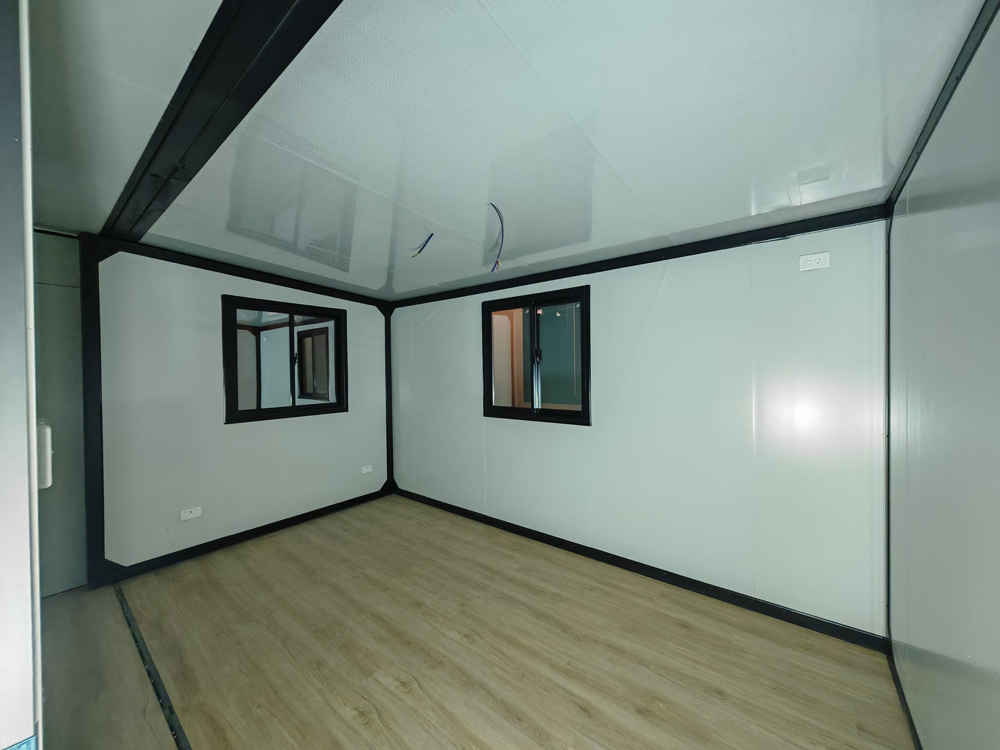 Small room with white walls, a wooden floor, and two small windows.