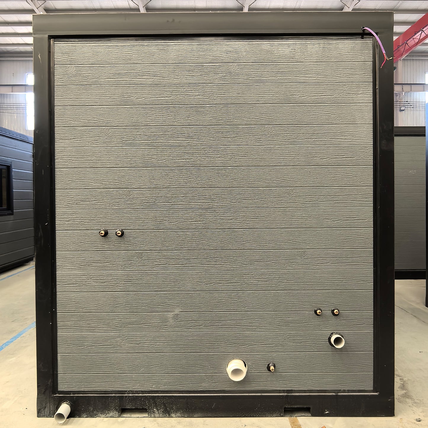 Portable bathroom with grey black, hot and cold water pipe interfaces at a side, with a pair of forklift holes for easy lifting