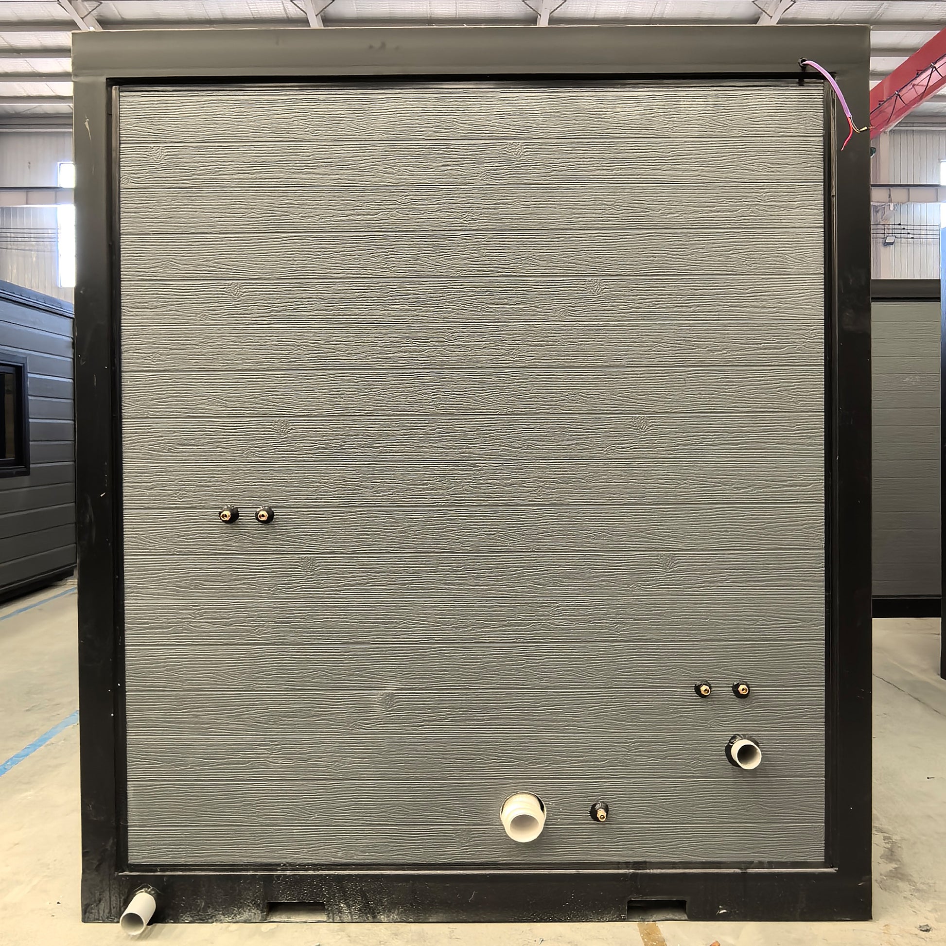 Portable bathroom with grey black, hot and cold water pipe interfaces at a side, with a pair of forklift holes for easy lifting