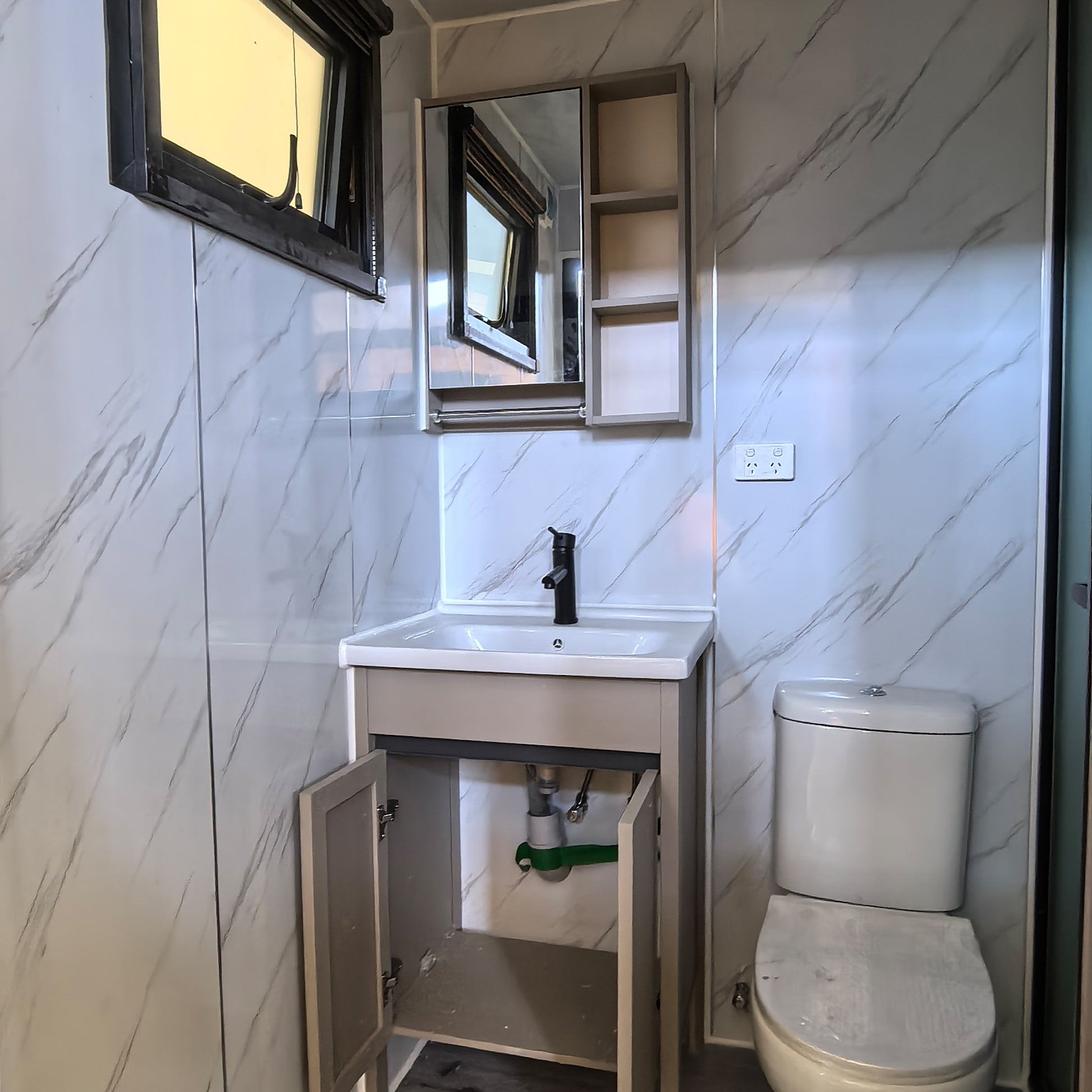 Small bathroom with toilet, sink, and mirror on a tiled wall.