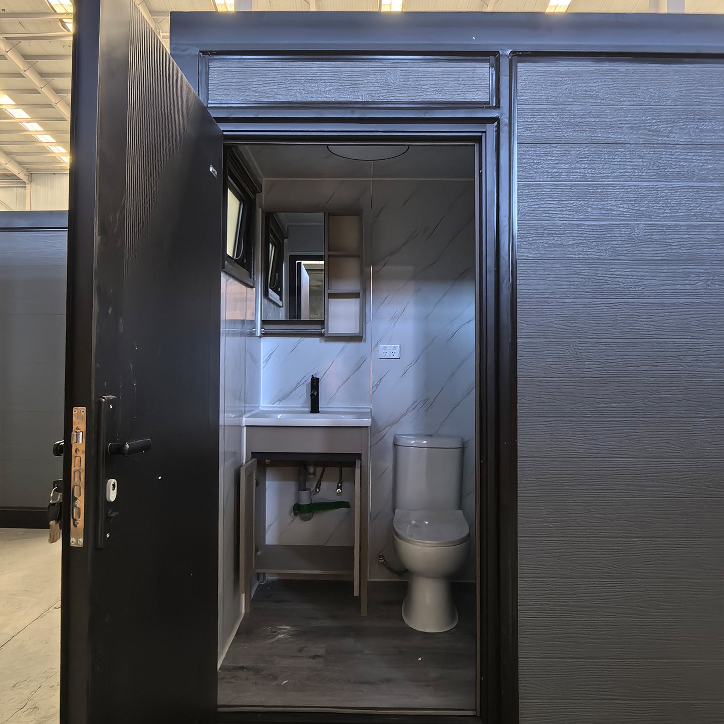 Compact bathroom with toilet and sink inside a black-framed enclosure.