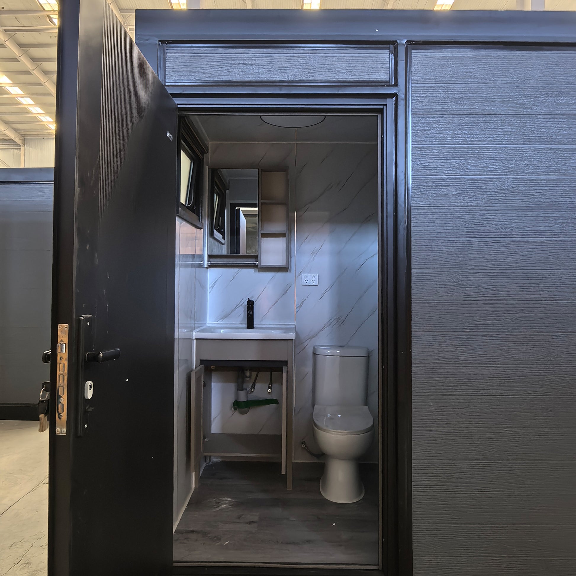 Compact bathroom with toilet and sink inside a black-framed enclosure.