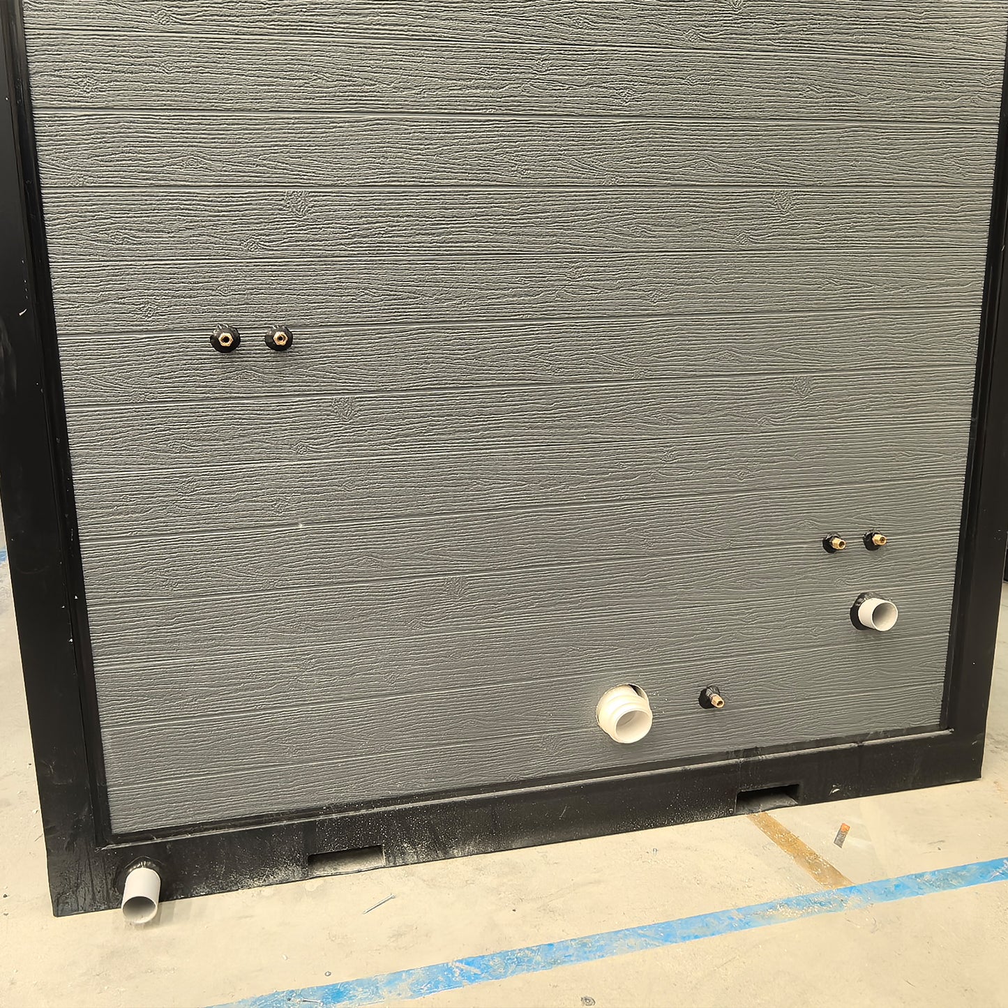 Gray textured panel with small pipes and fixtures on a concrete floor