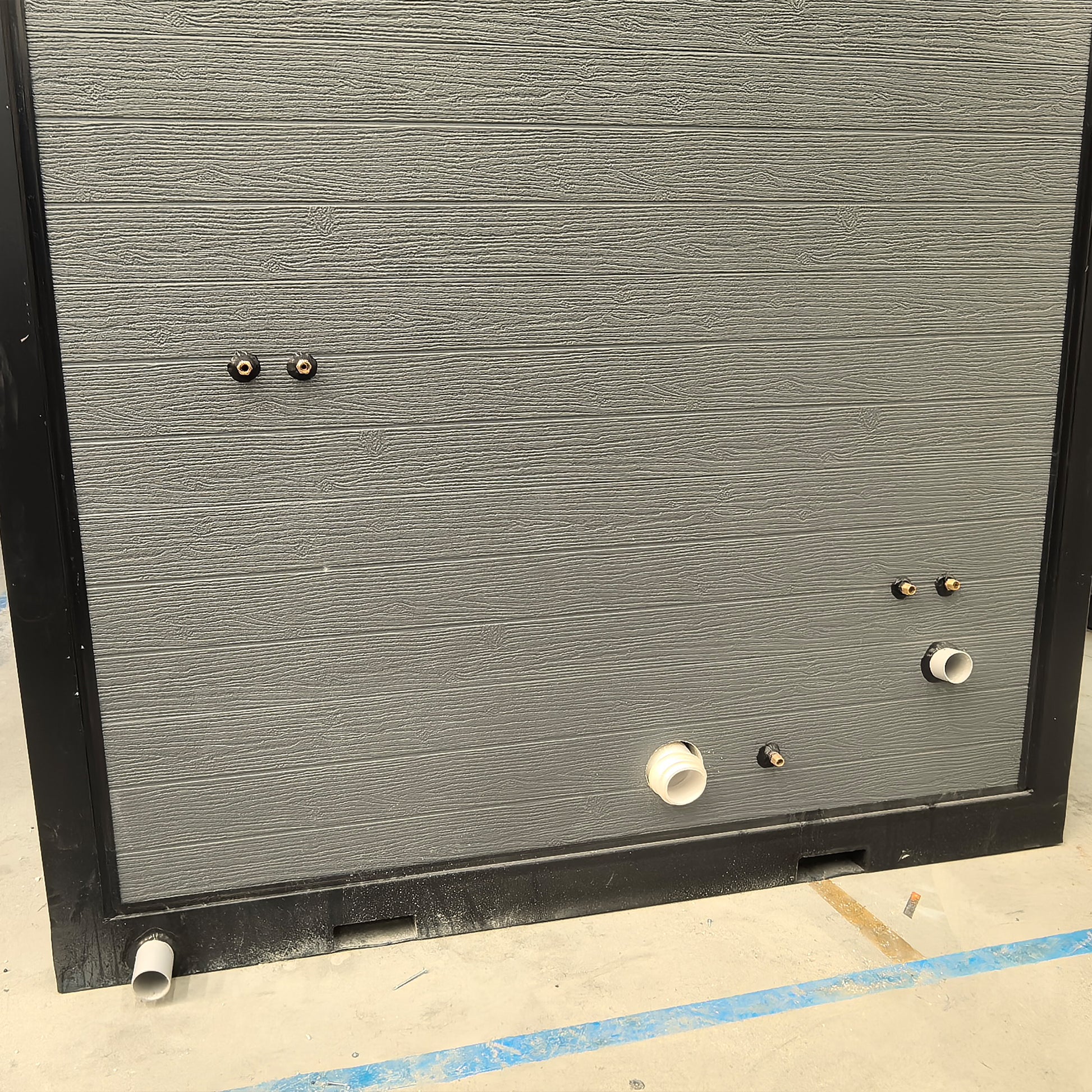 Gray textured panel with small pipes and fixtures on a concrete floor