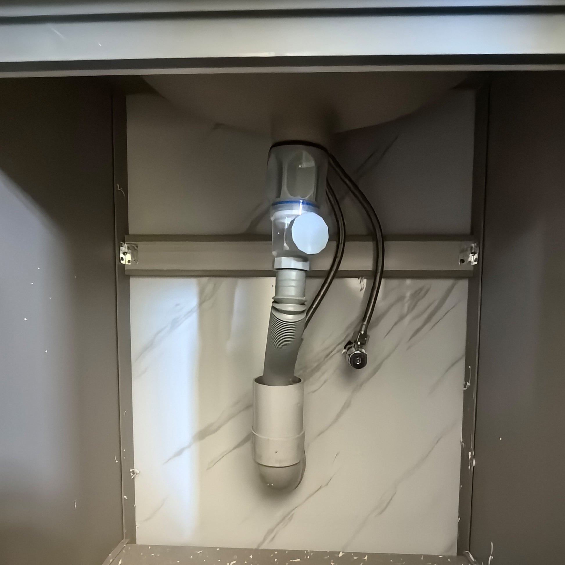 Under-sink plumbing setup with pipes and valve on a marble countertop.